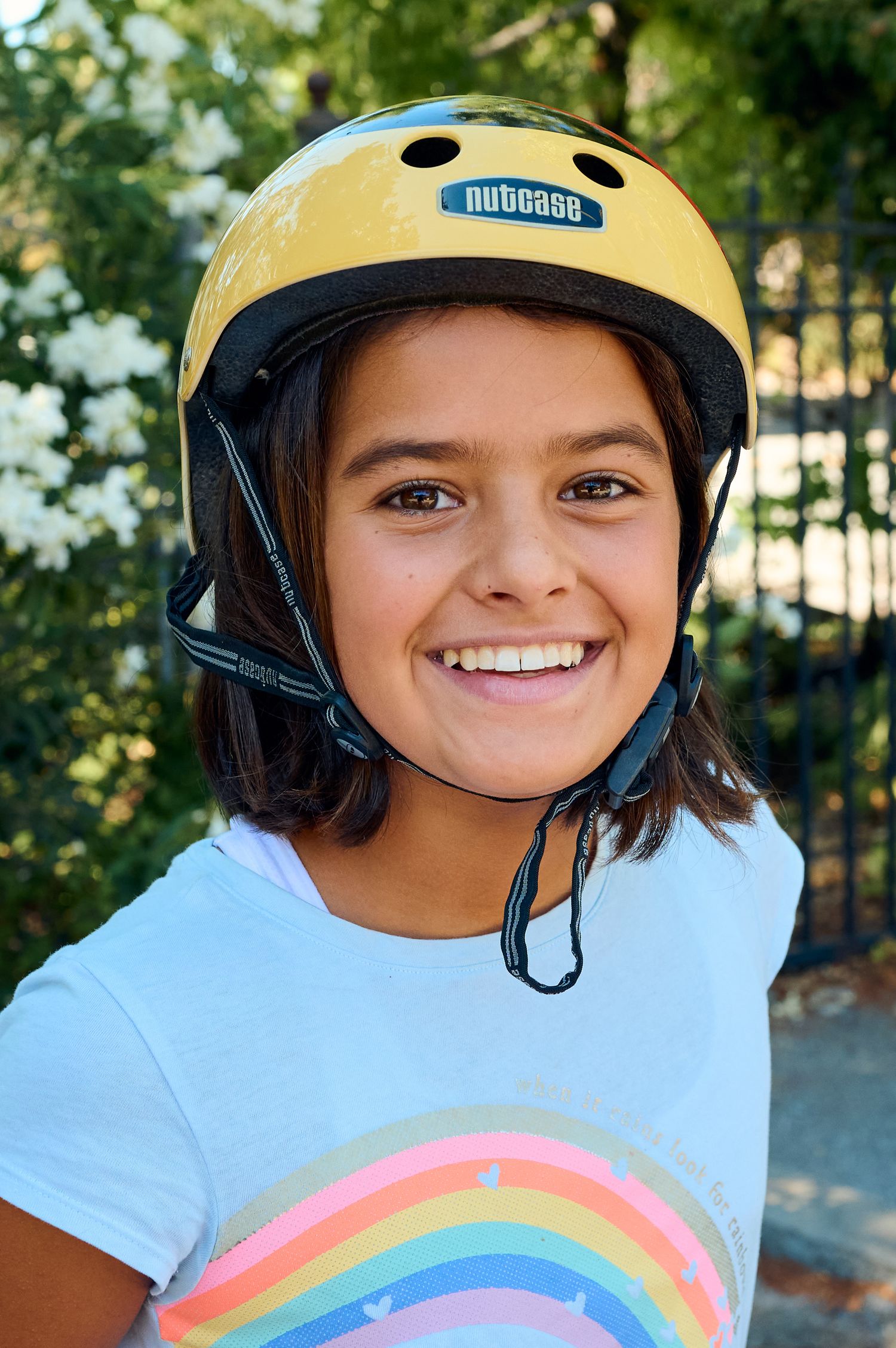 A person wearing a yellow safety helmet and rainbow shirt smiles outdoors.