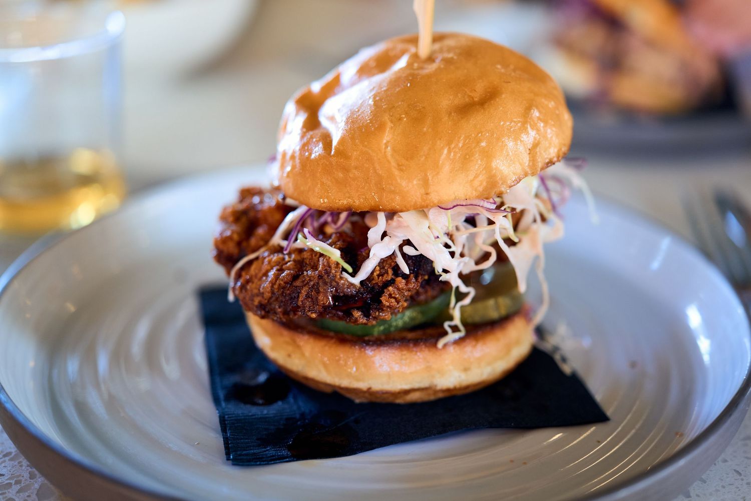 Gourmet burger with shredded cabbage and sauce on brioche bun served on white plate.