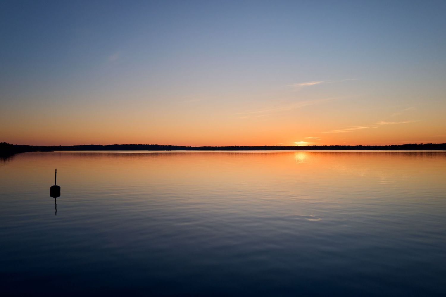 Single buoy floating on perfectly still lake water during golden sunset.