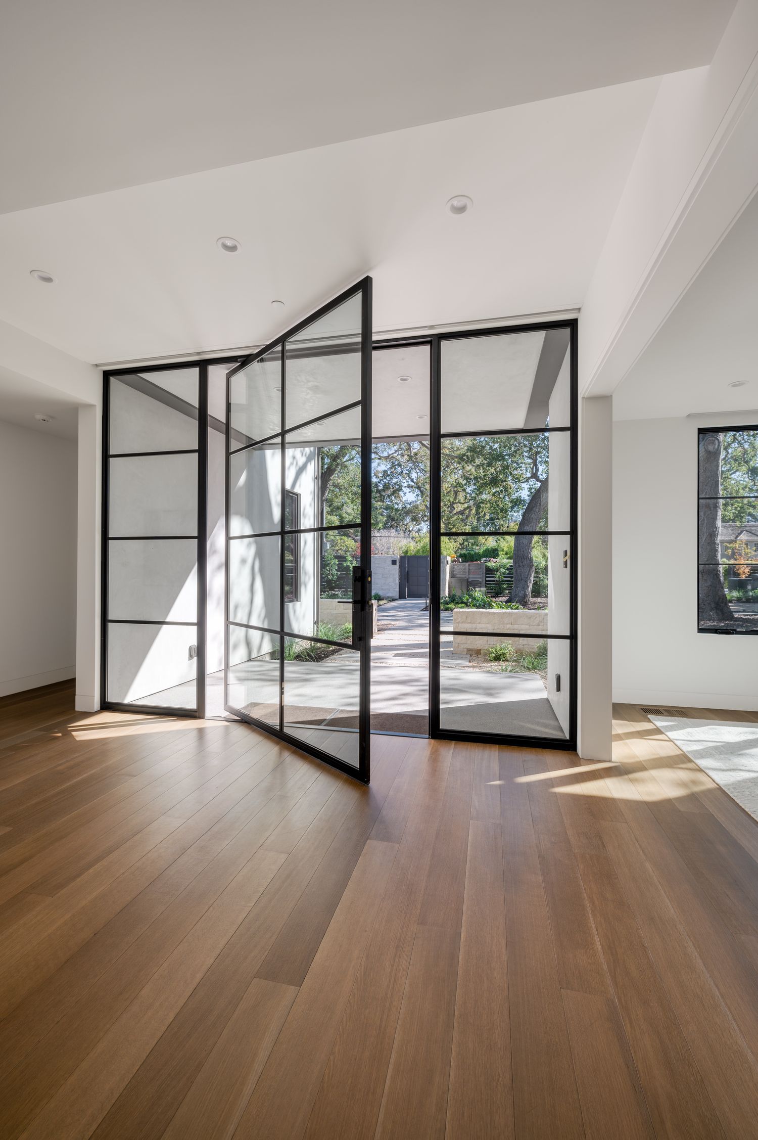 Elegant living space with large steel-framed glass doors, vaulted ceiling, and wide plank hardwood flooring.