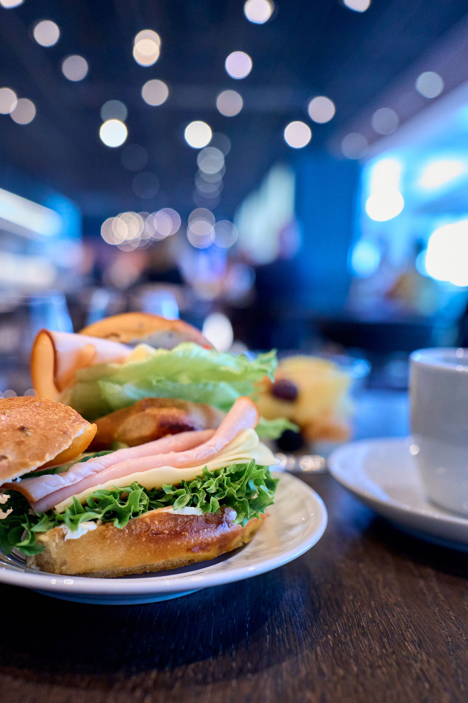A fresh deli sandwich with lettuce and meat on a plate with blurred blue lights in the background.