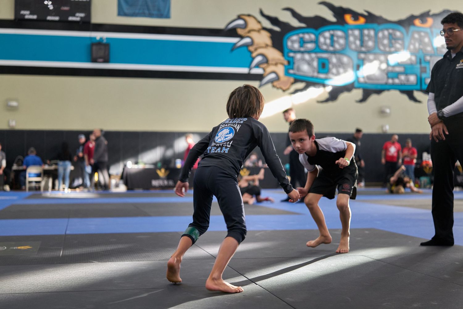 Two competitors in black gis face off during a Brazilian jiu-jitsu competition match.