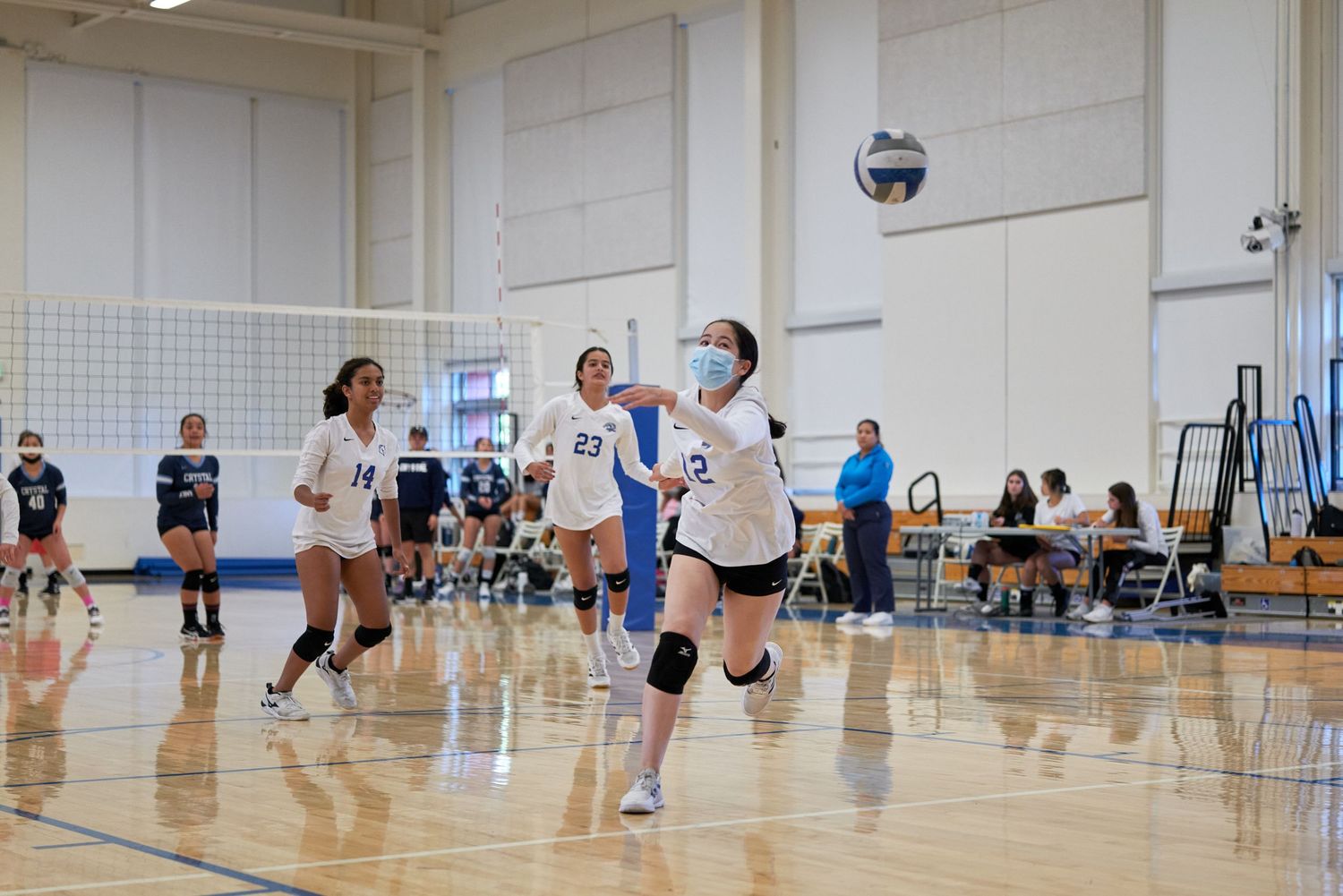 Players positioned on volleyball court during indoor match with net in foreground.
