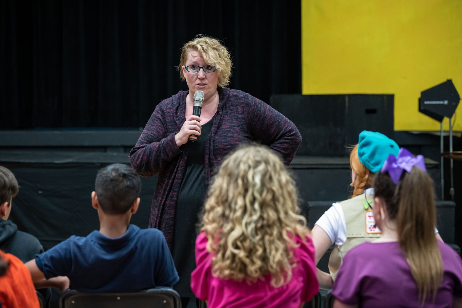 A speaker addresses an audience of students in an auditorium setting.