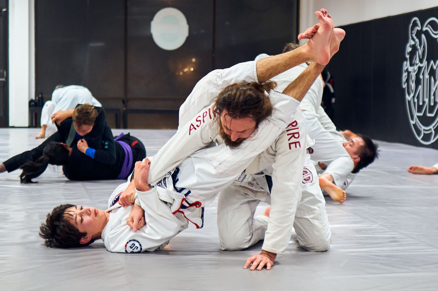Two practitioners in white gis practicing Brazilian jiu-jitsu techniques on the mat.