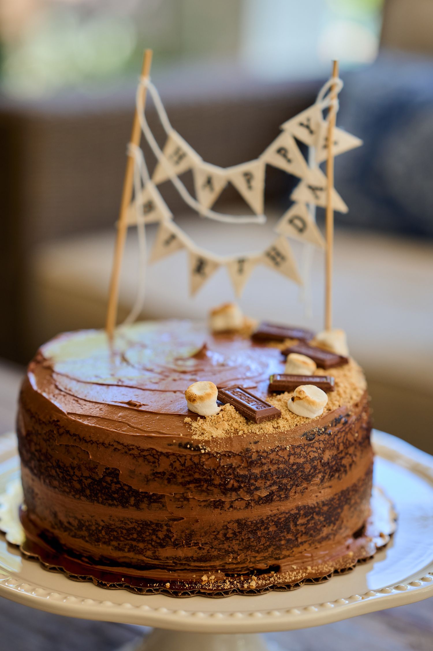Chocolate layer cake with rustic frosting decorated with a handmade banner topper on white plate.