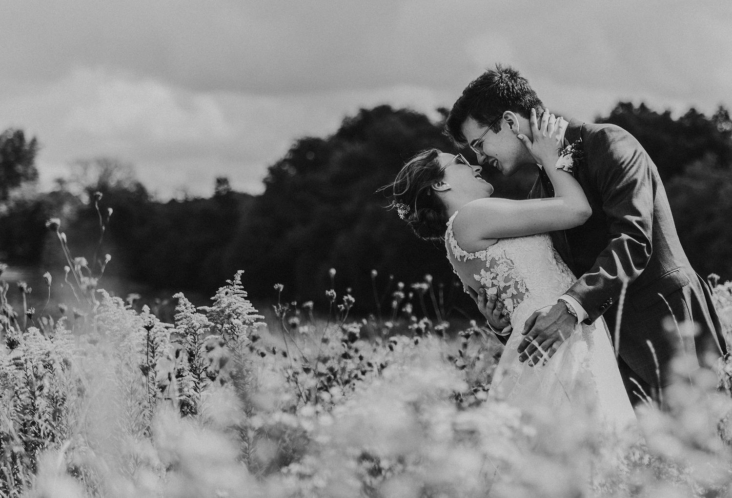 A couple embraces romantically in a dreamy black and white field of wildflowers on an overcast day.