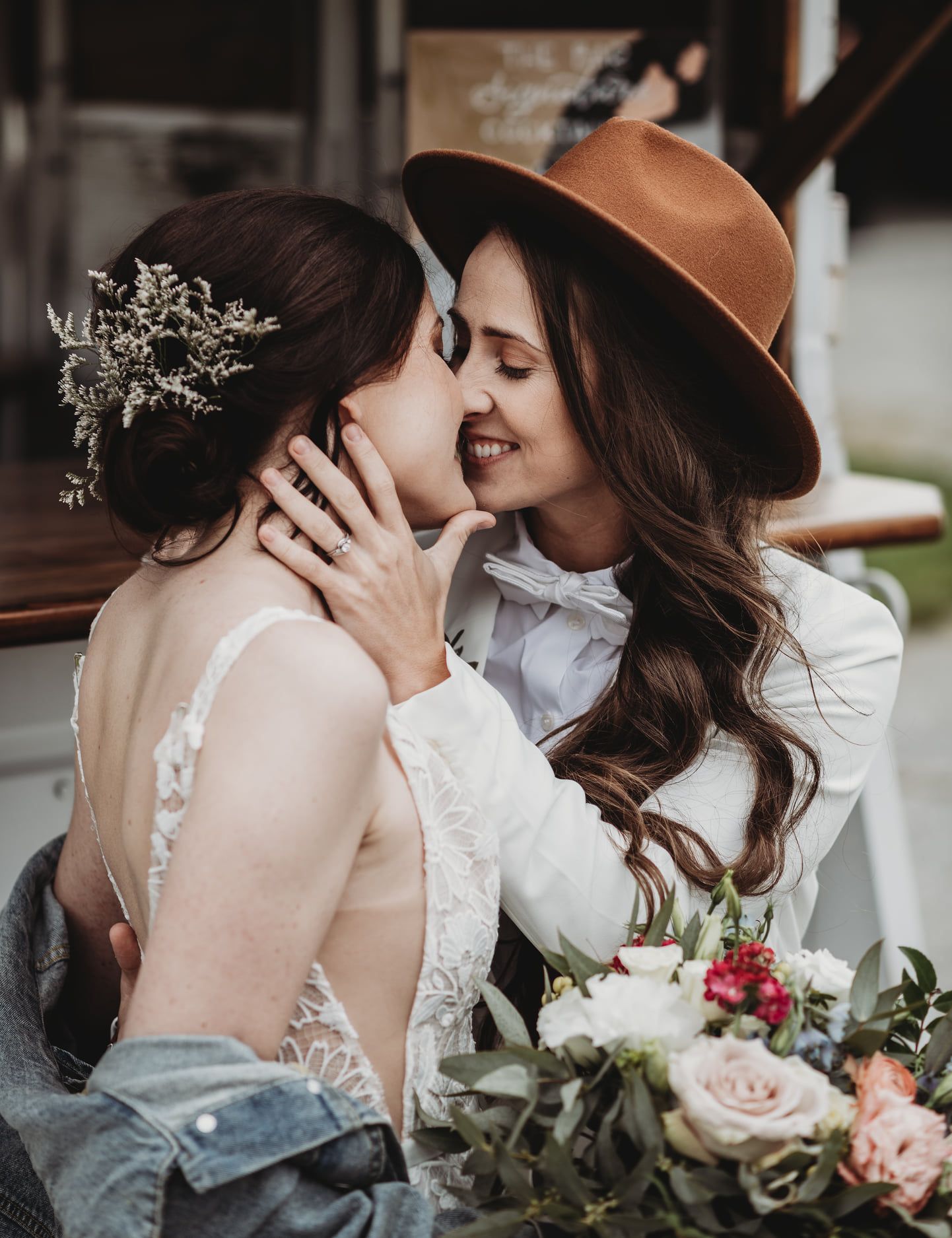 A romantic moment between two brides sharing a tender kiss while holding a bouquet of pink and white roses at their wedding.