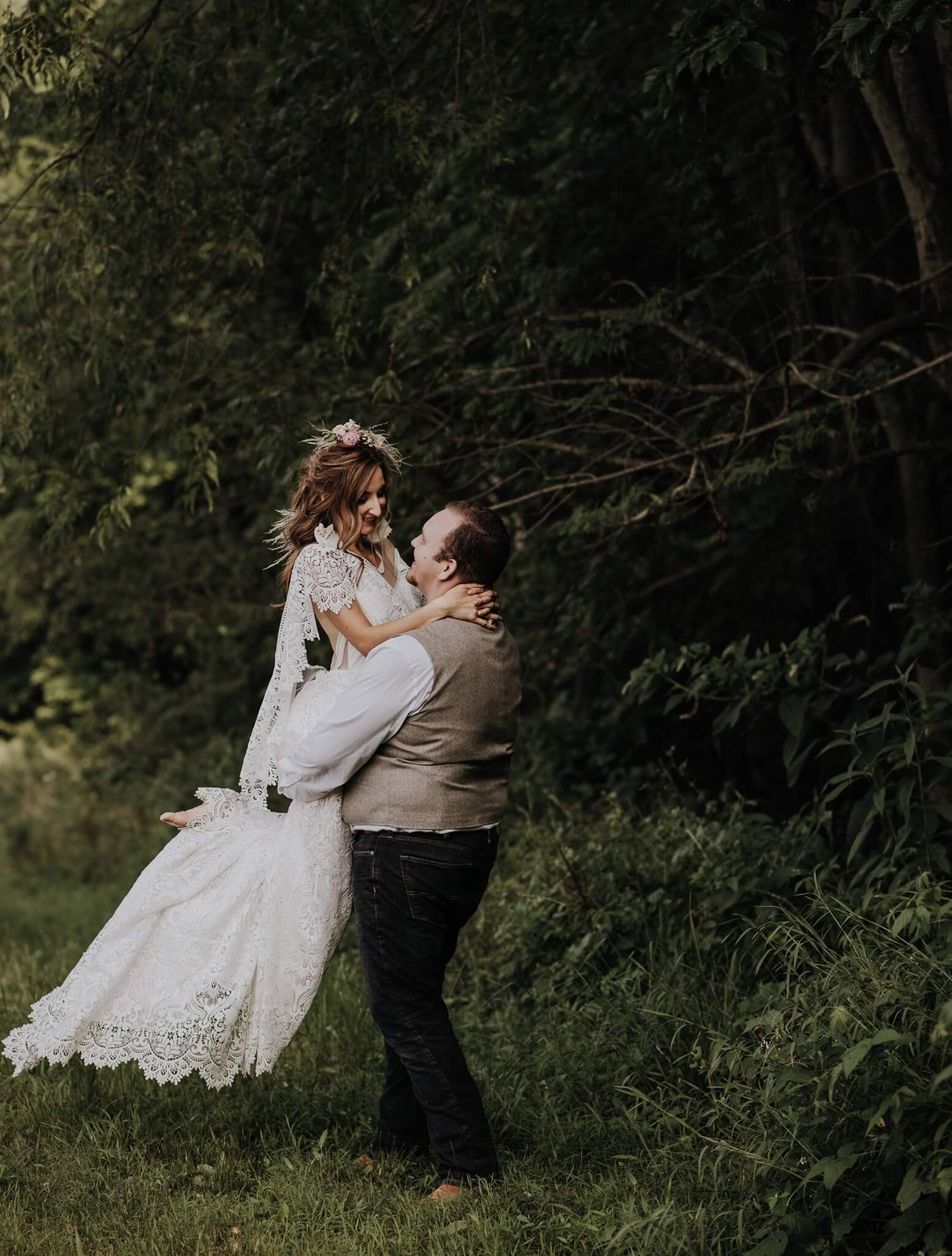 A couple in traditional wedding attire dance and embrace in a romantic outdoor setting with lush greenery.