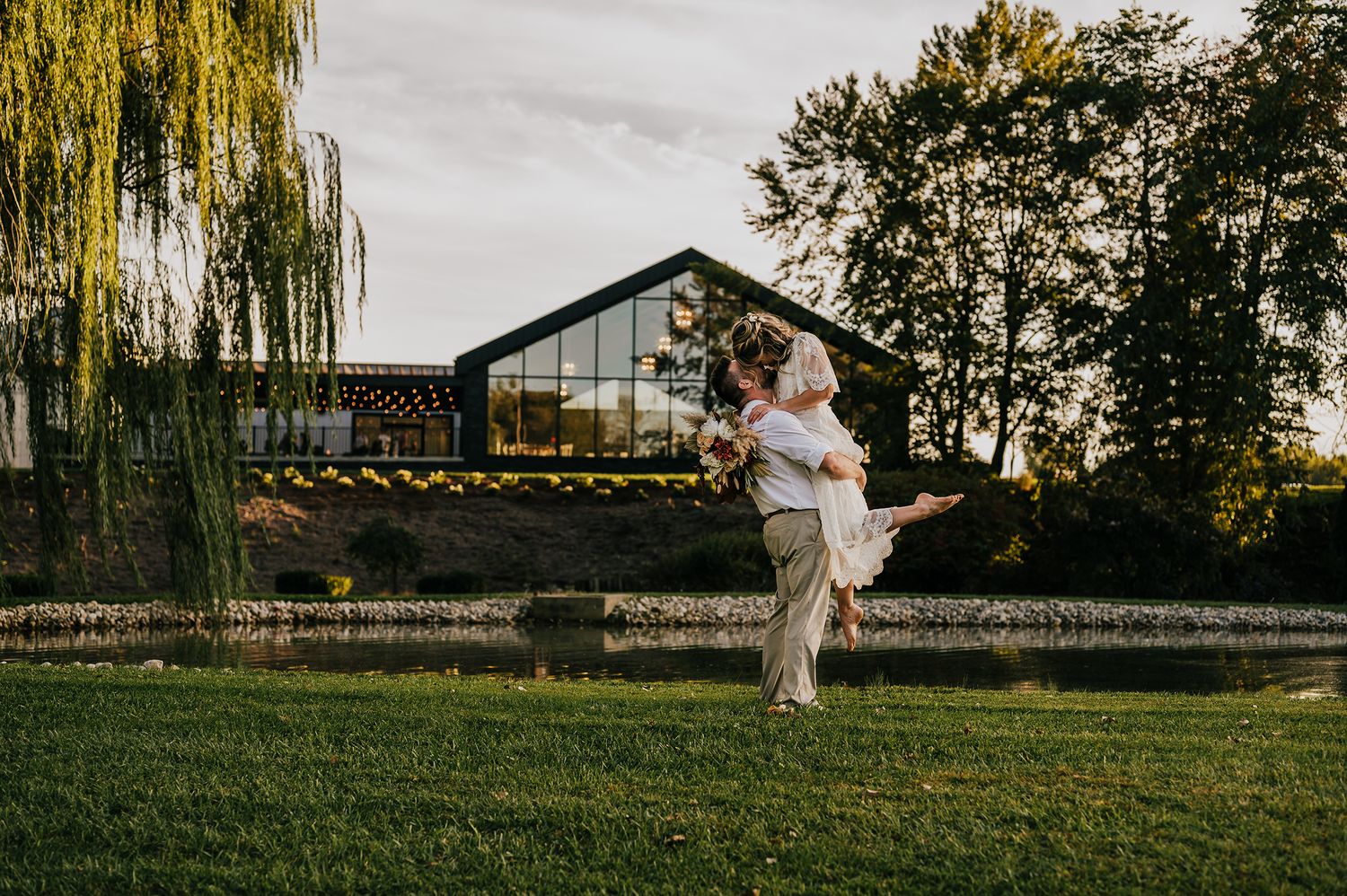 A woman in a flowy white dress twirls gracefully in a grassy field at sunset with trees in the background.