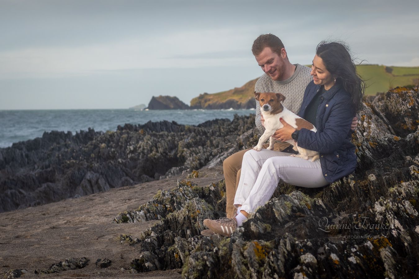 Couple and their dog sitting on the rocks at Owenehinca beach during a Couple photoshoot