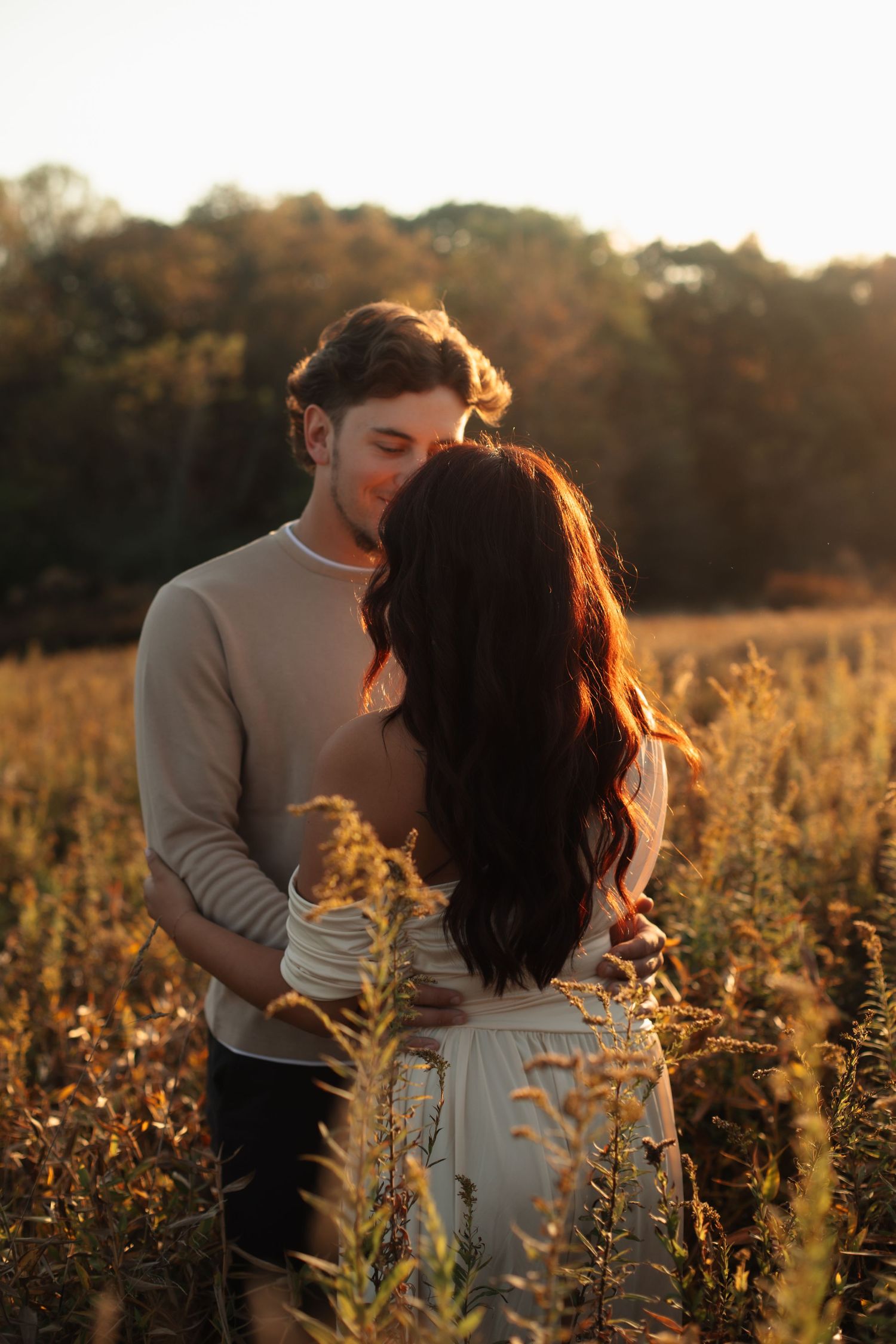 A romantic couple embraces in a golden sunlit meadow at sunset.