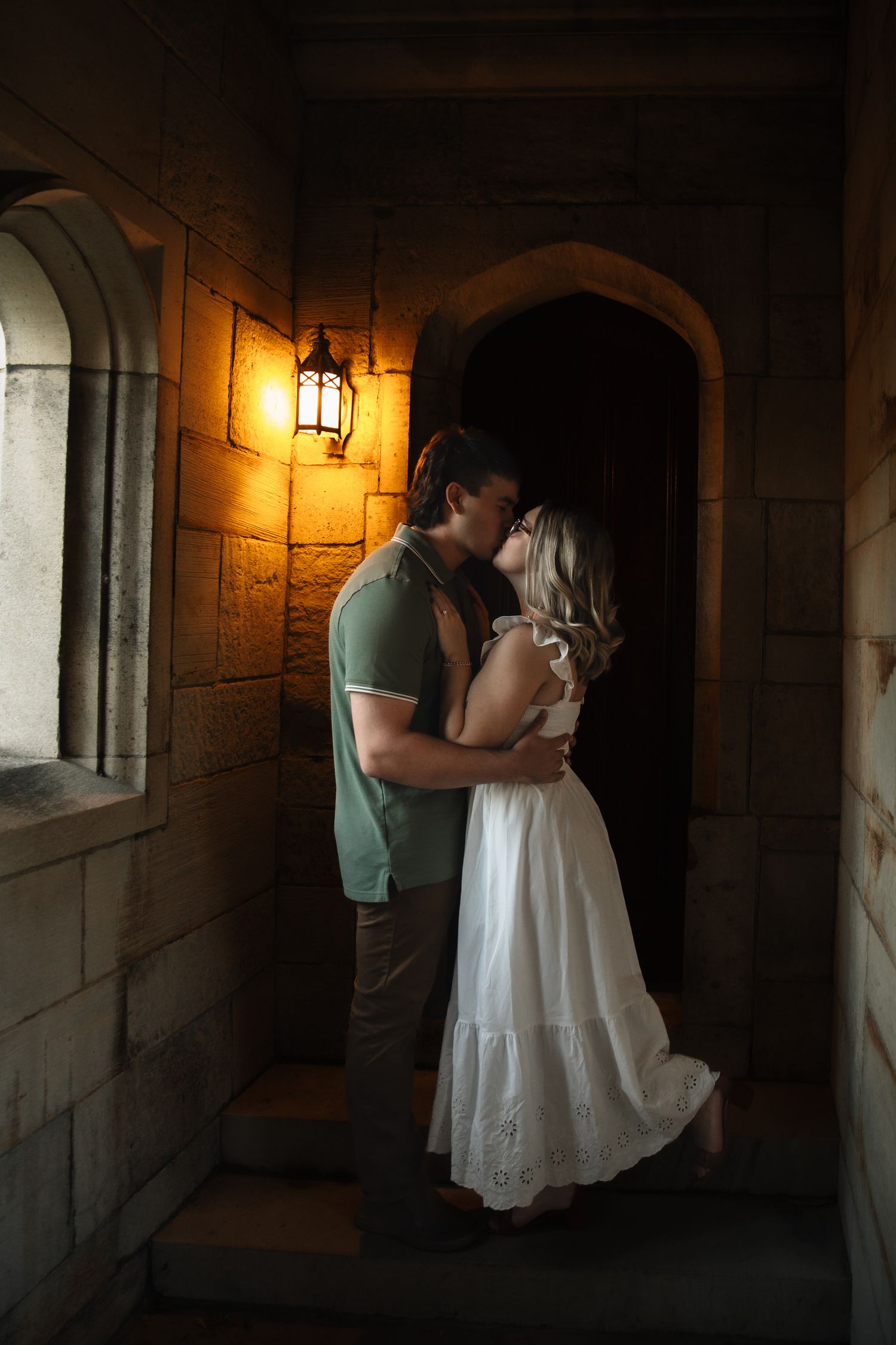 Romantic couple embracing in a dimly lit stone hallway with warm glowing lanterns.