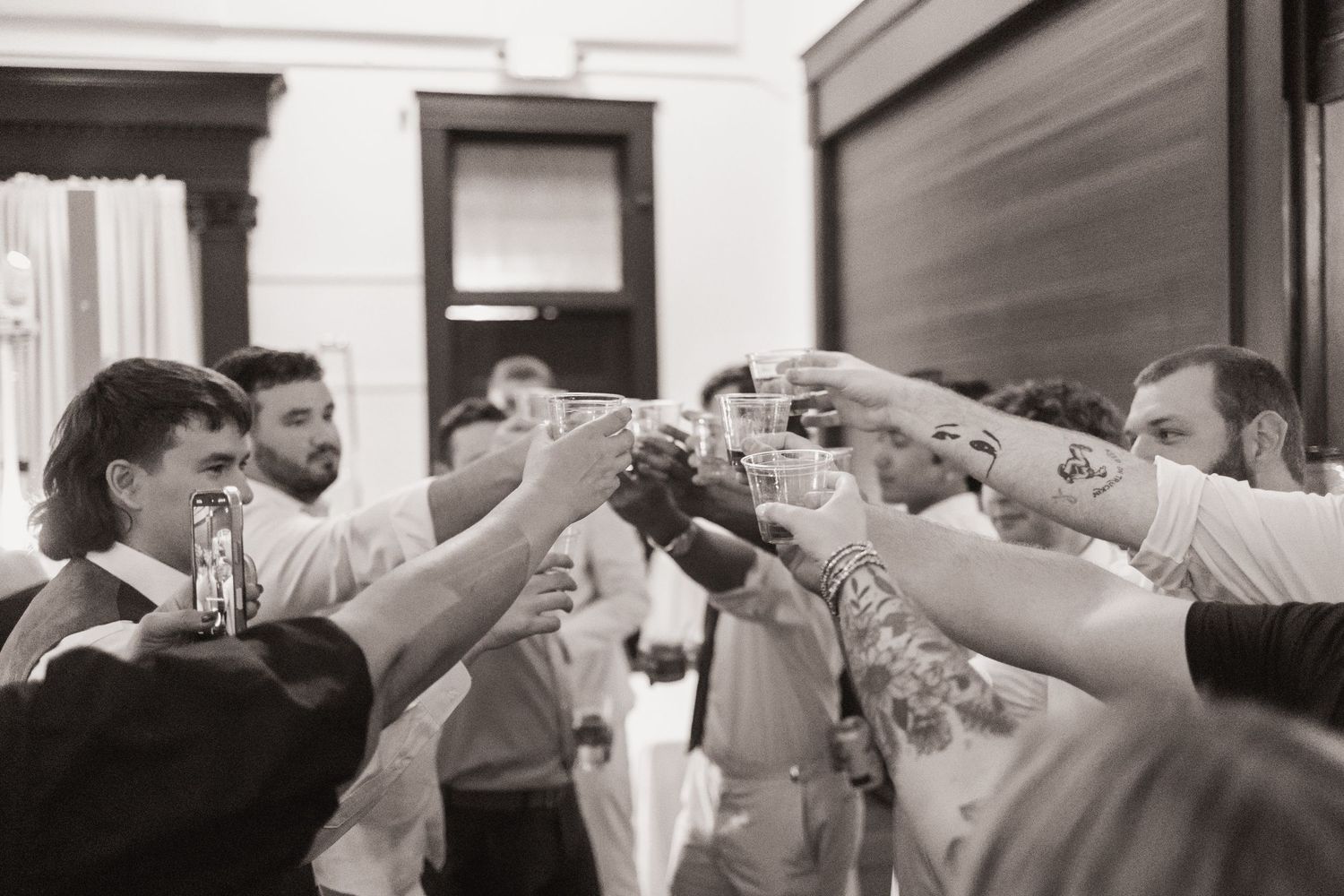 Black and white photo of groomsmen raising glasses in a celebratory toast at a wedding reception.