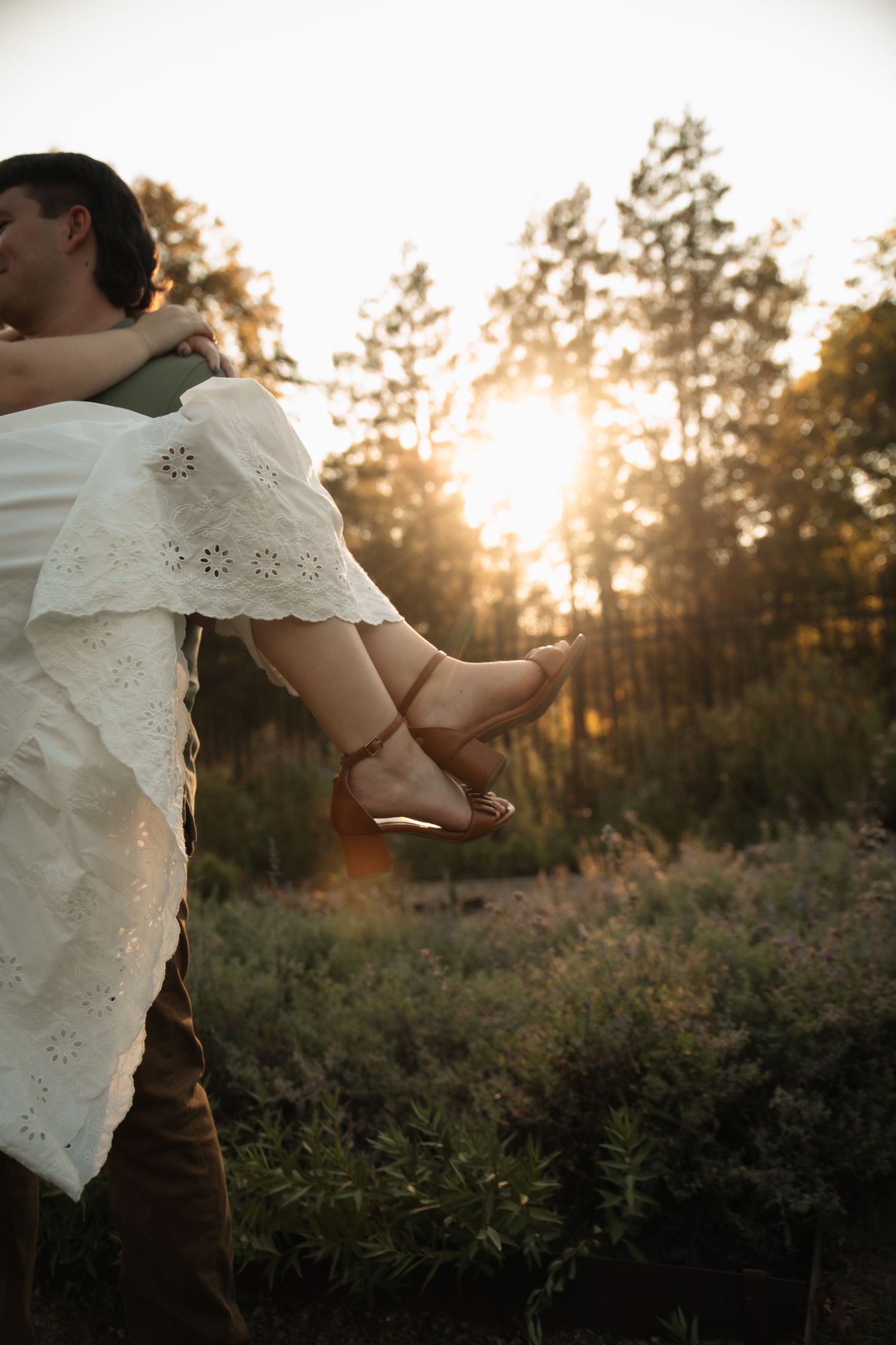 A person in a white lace dress stands in a golden sunset field with trees silhouetted in the background.