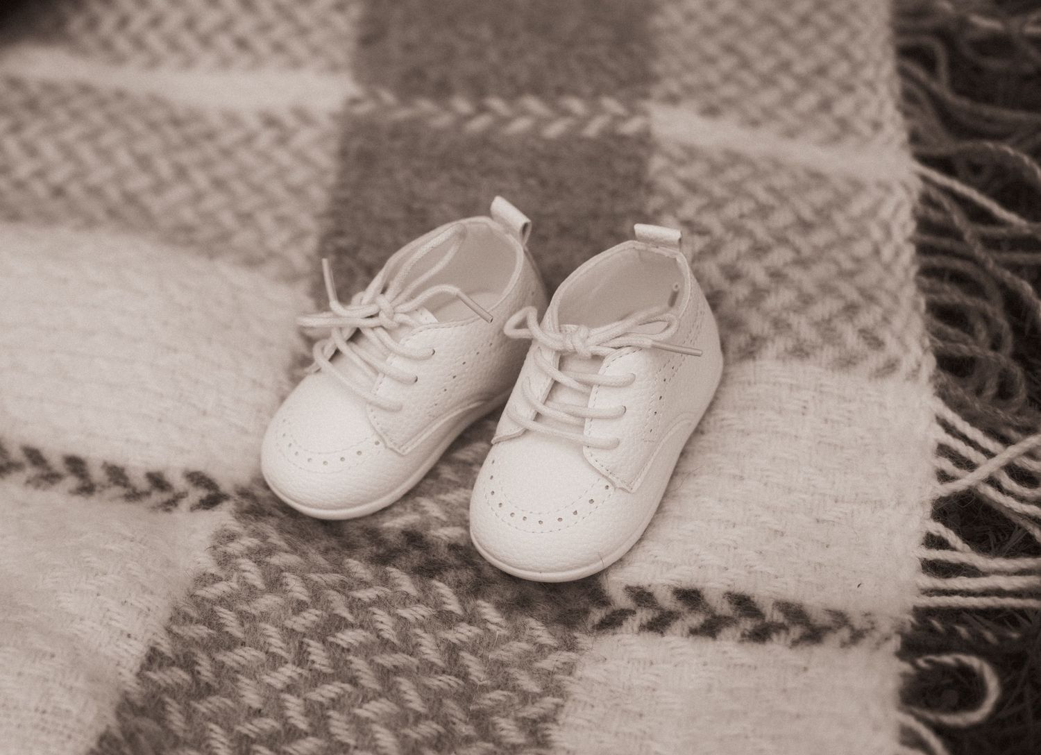 Row of small white baby shoes arranged on a gray and white checkered blanket showing progression.