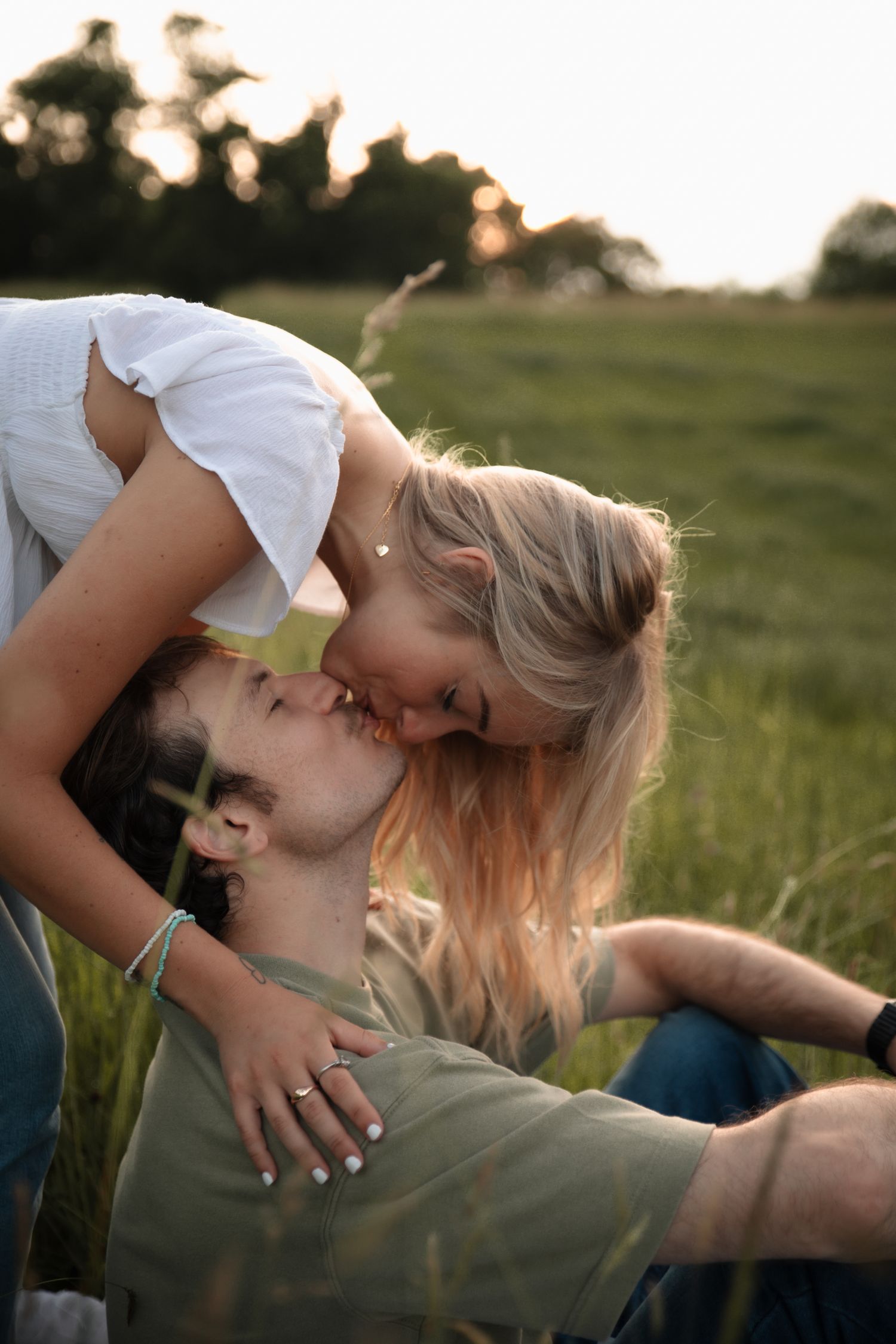 A couple sharing an intimate moment lying in a grassy field at sunset.