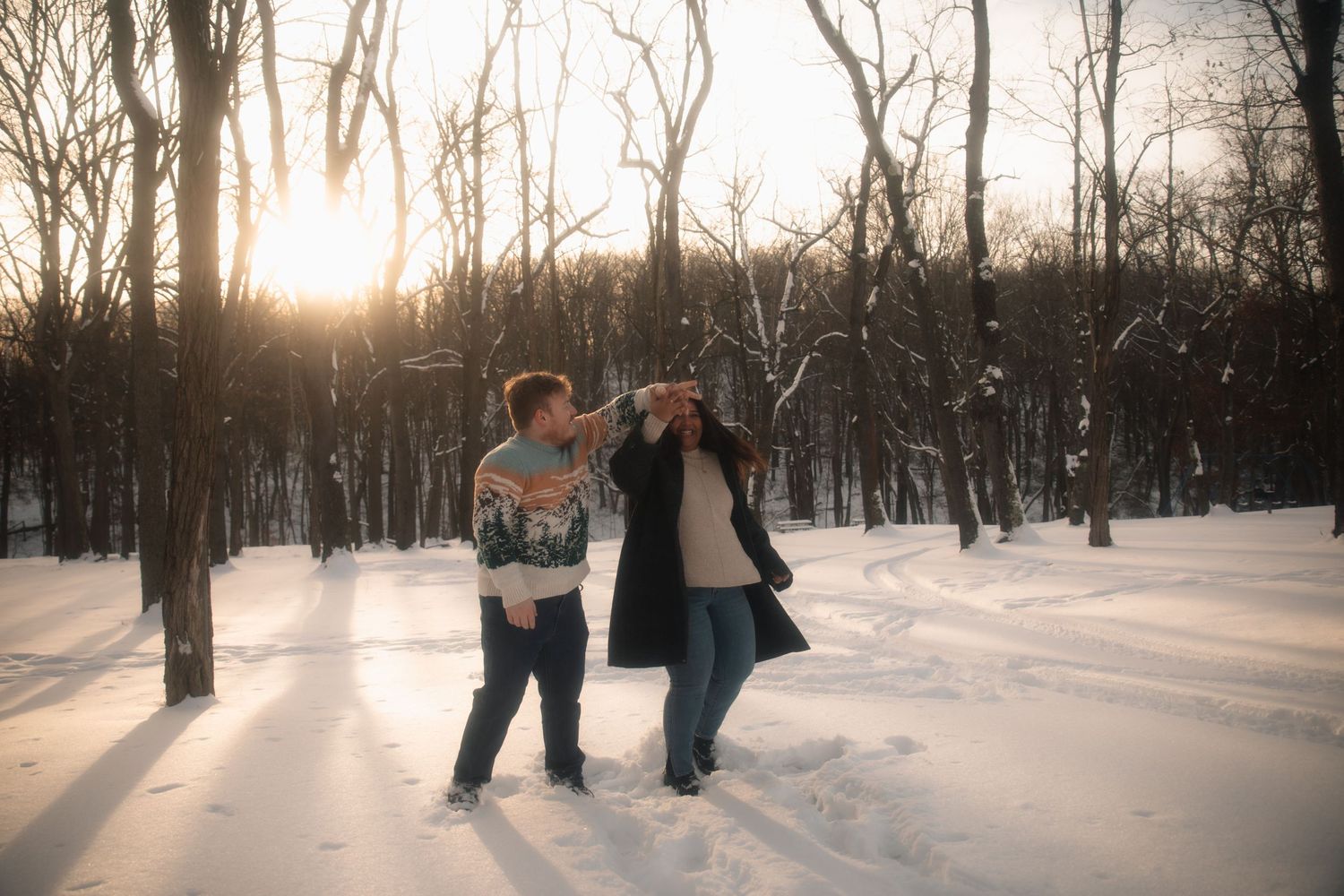 People walking through a snowy winter park at sunset with long shadows cast on the pristine white ground.