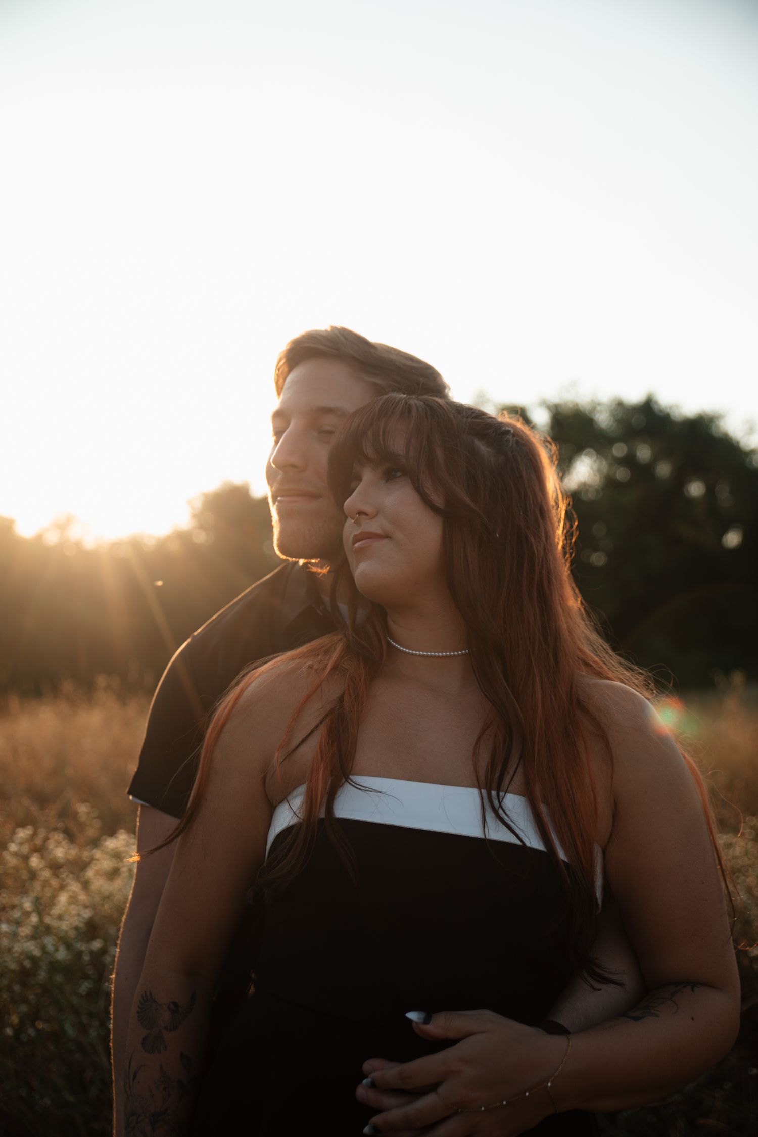 A romantic couple embraces in a sunlit field during golden hour as warm light filters through their silhouettes.