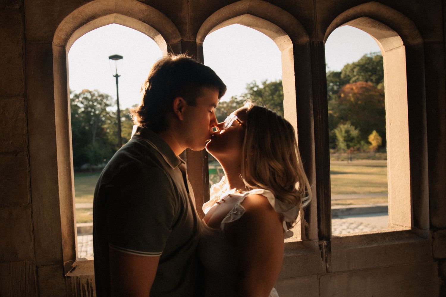 A silhouetted couple shares an intimate moment in front of a window during golden hour.