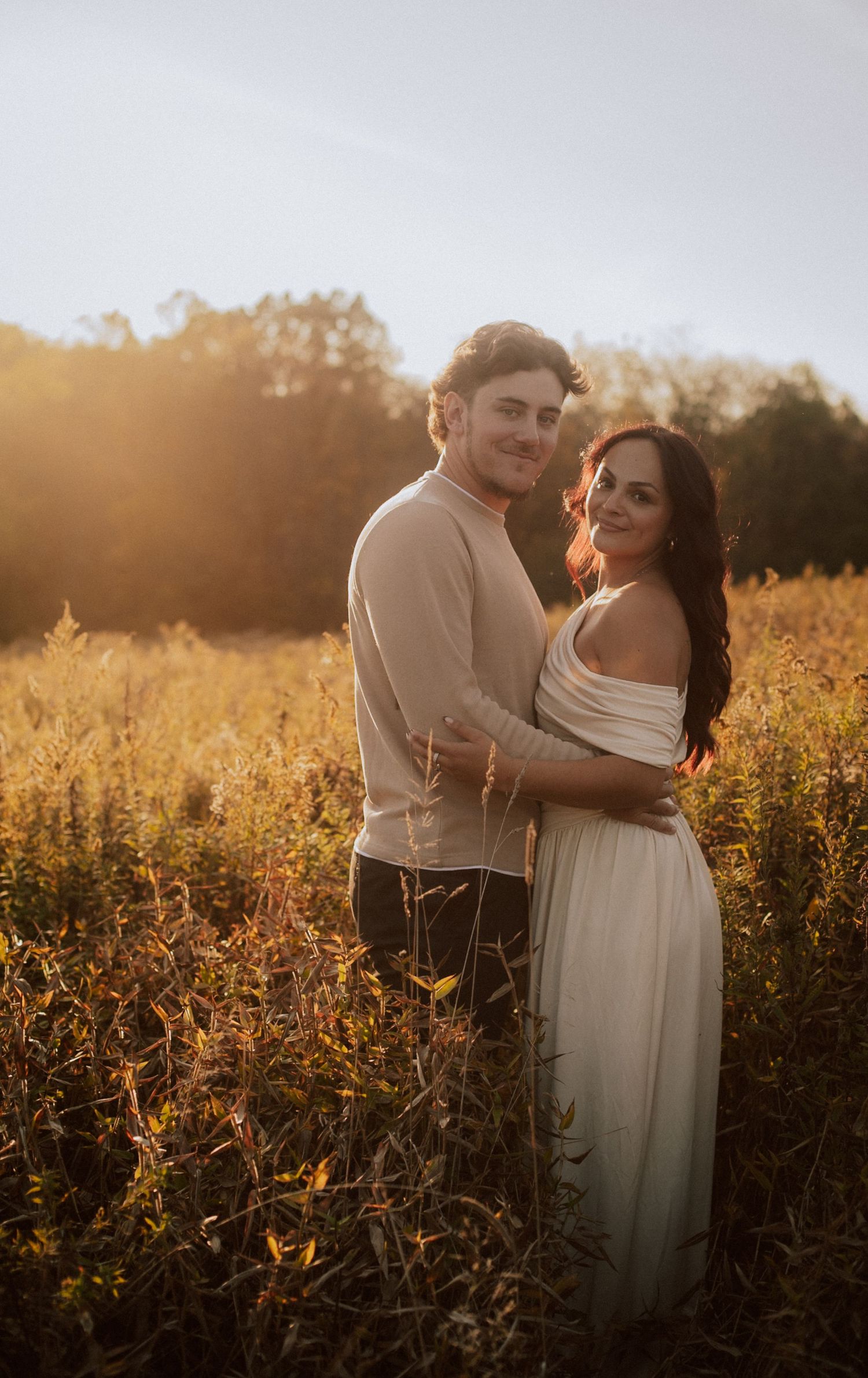 A couple embraces in a golden field at sunset creating a romantic silhouette against the warm evening light.