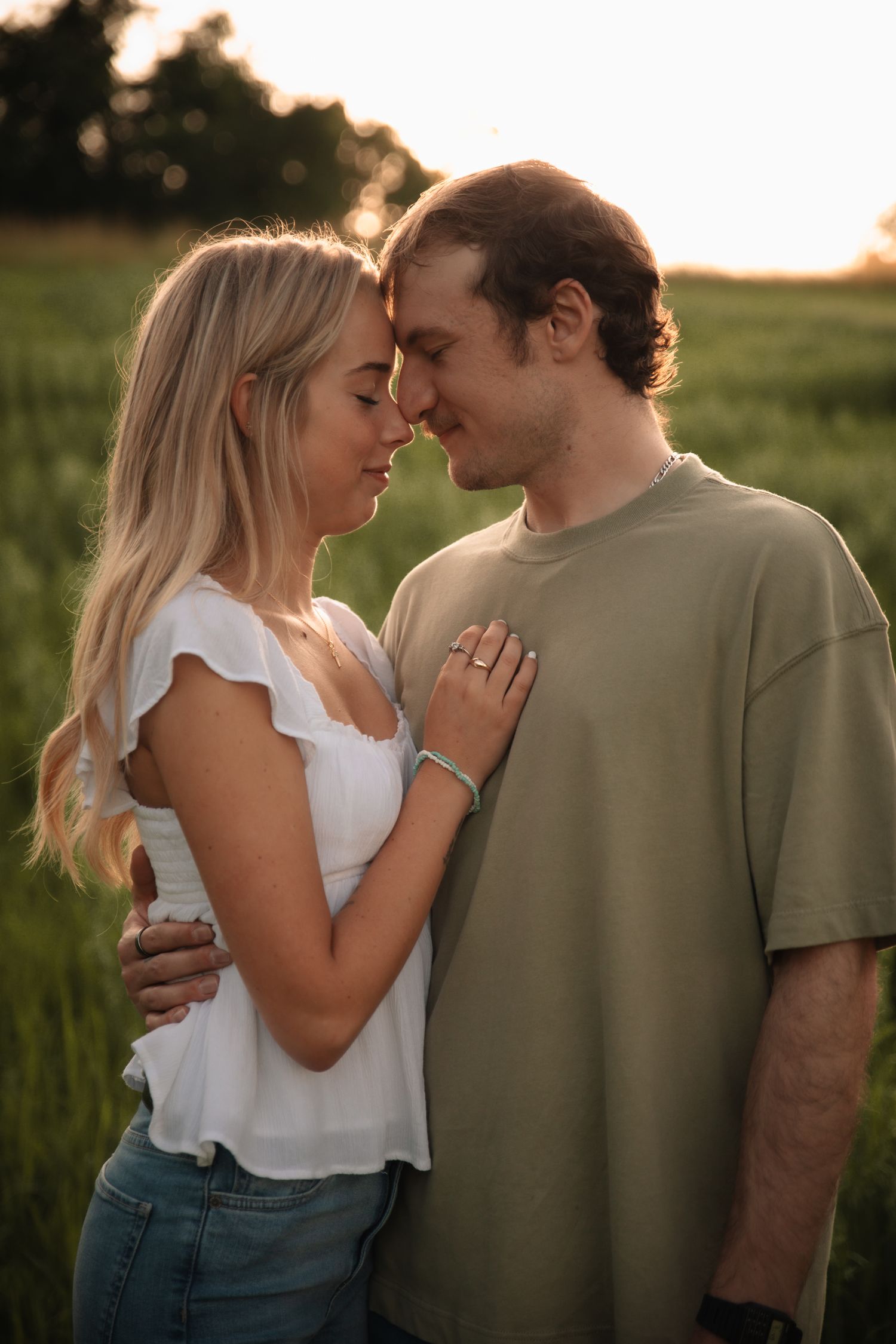 A romantic couple shares intimate moments at sunset in a grassy field wearing casual summer attire.