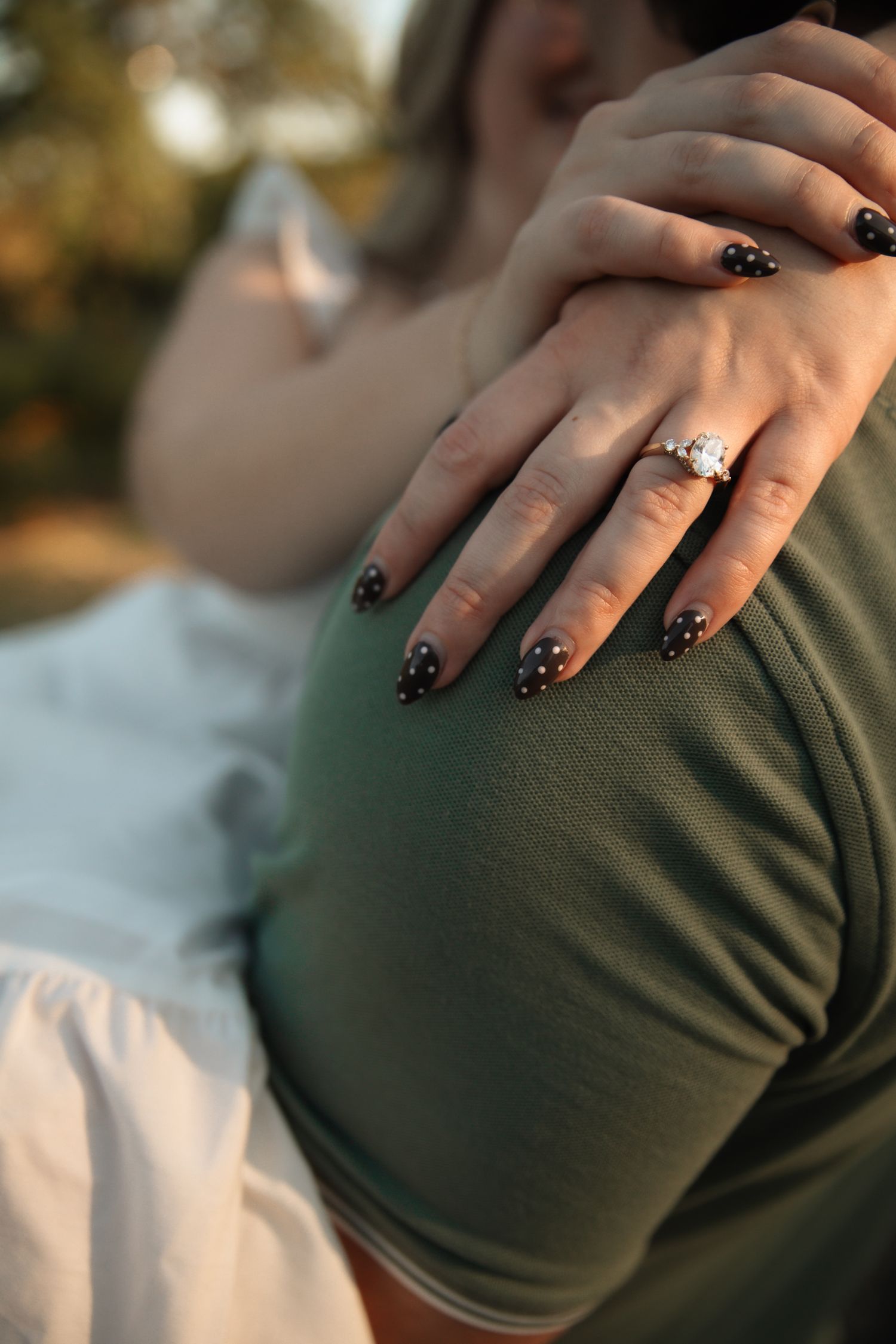 Close-up of hands with black sparkly nail polish against a dark green sweater.