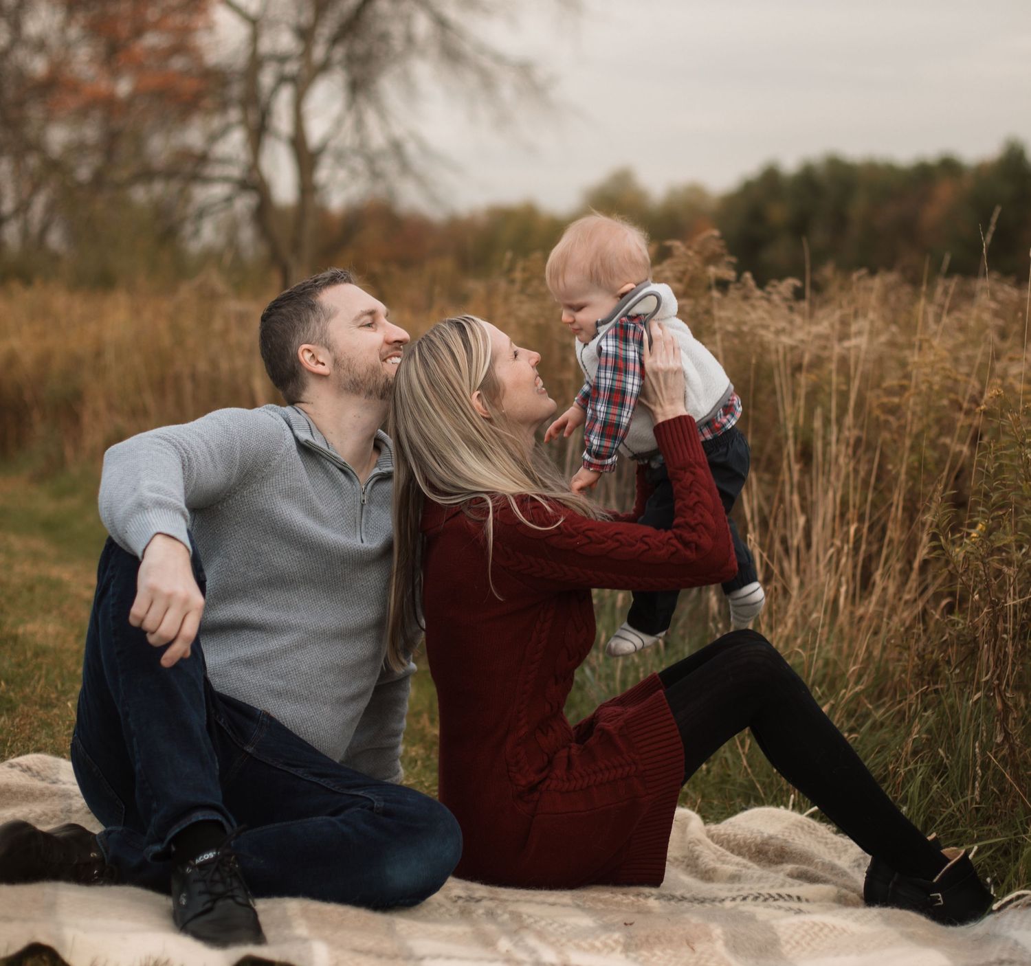 Couple laying in tall autumn grass enjoying a playful moment together in a field at sunset.