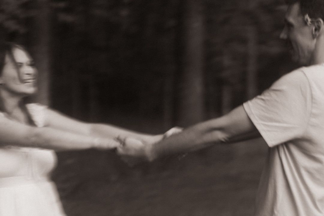 Couple holding hands and spinning together outdoors in a blurred black and white romantic photo.