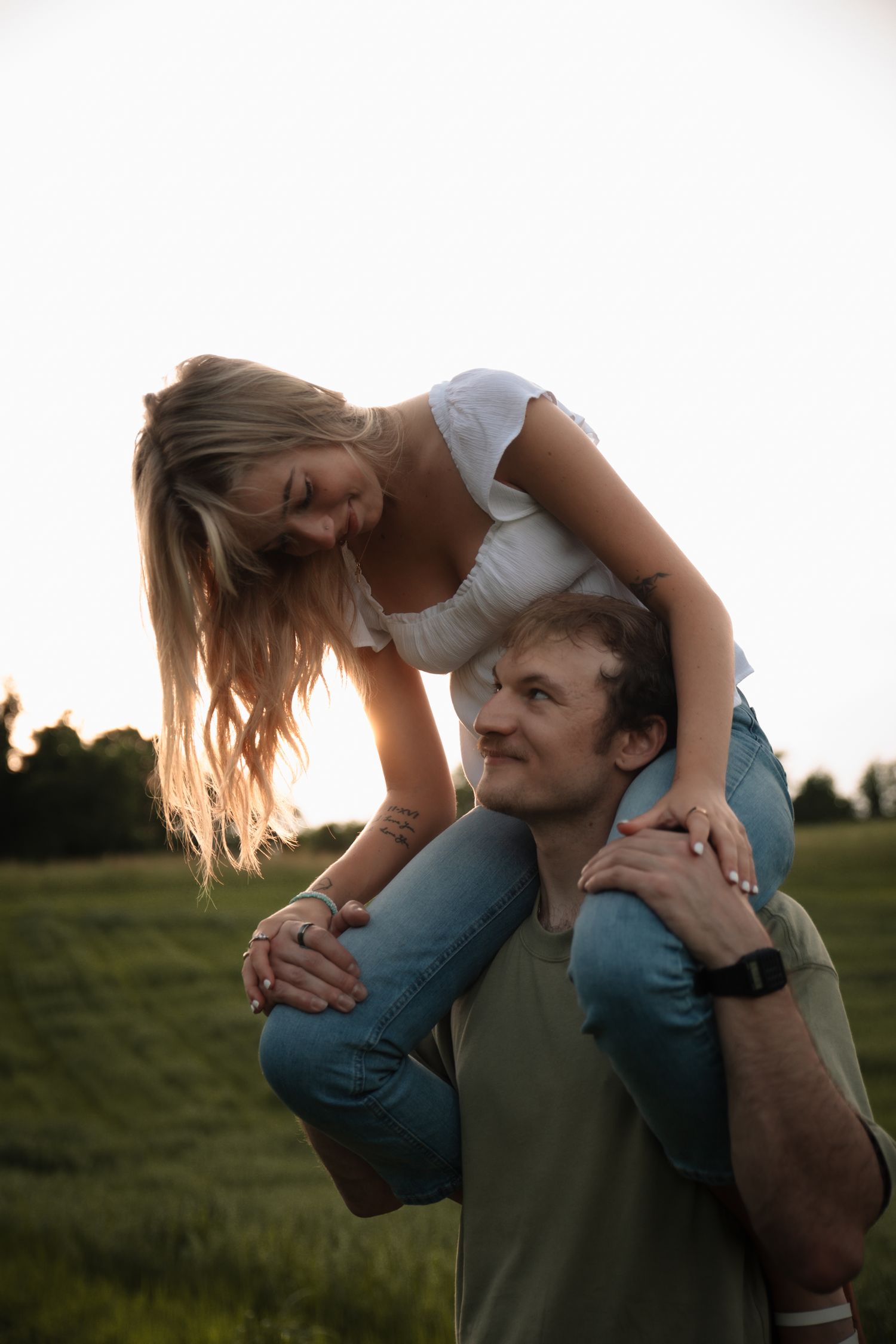 A couple shares a playful moment at sunset in a grassy field as they embrace and laugh together.