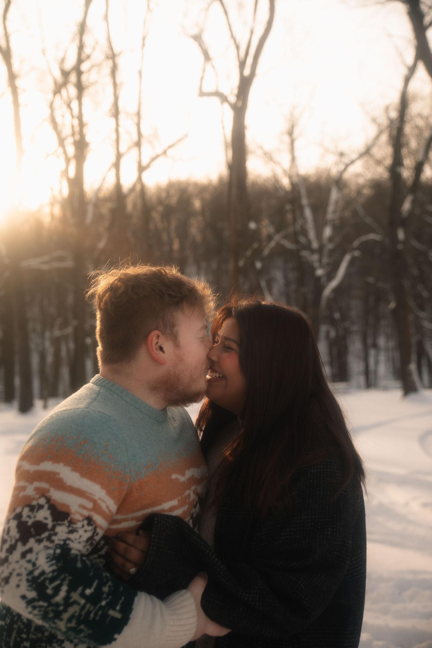 Romantic winter scene with couple sharing an intimate moment in a snowy forest at sunset.