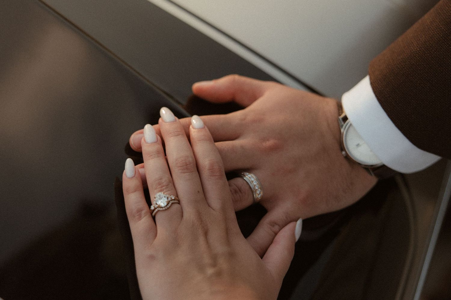 Close-up of couple's hands showing diamond engagement ring and wedding band, with man wearing a silver watch.