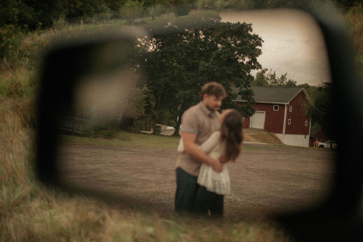 Couple embracing romantically reflected in a car side mirror with a red barn and trees in the background.