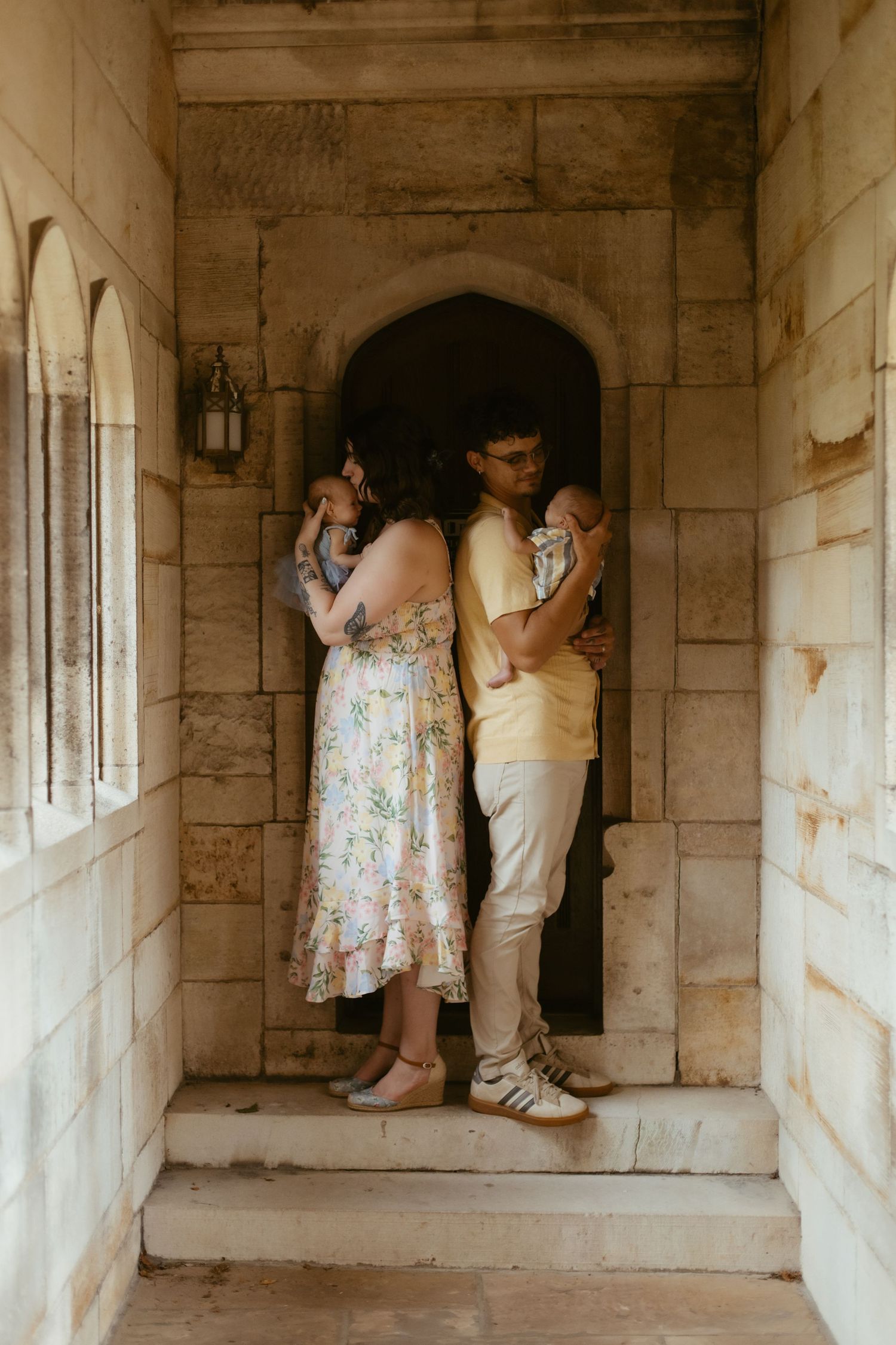 Couple embracing in a stone archway doorway, woman in floral dress and man in yellow shirt on steps.
