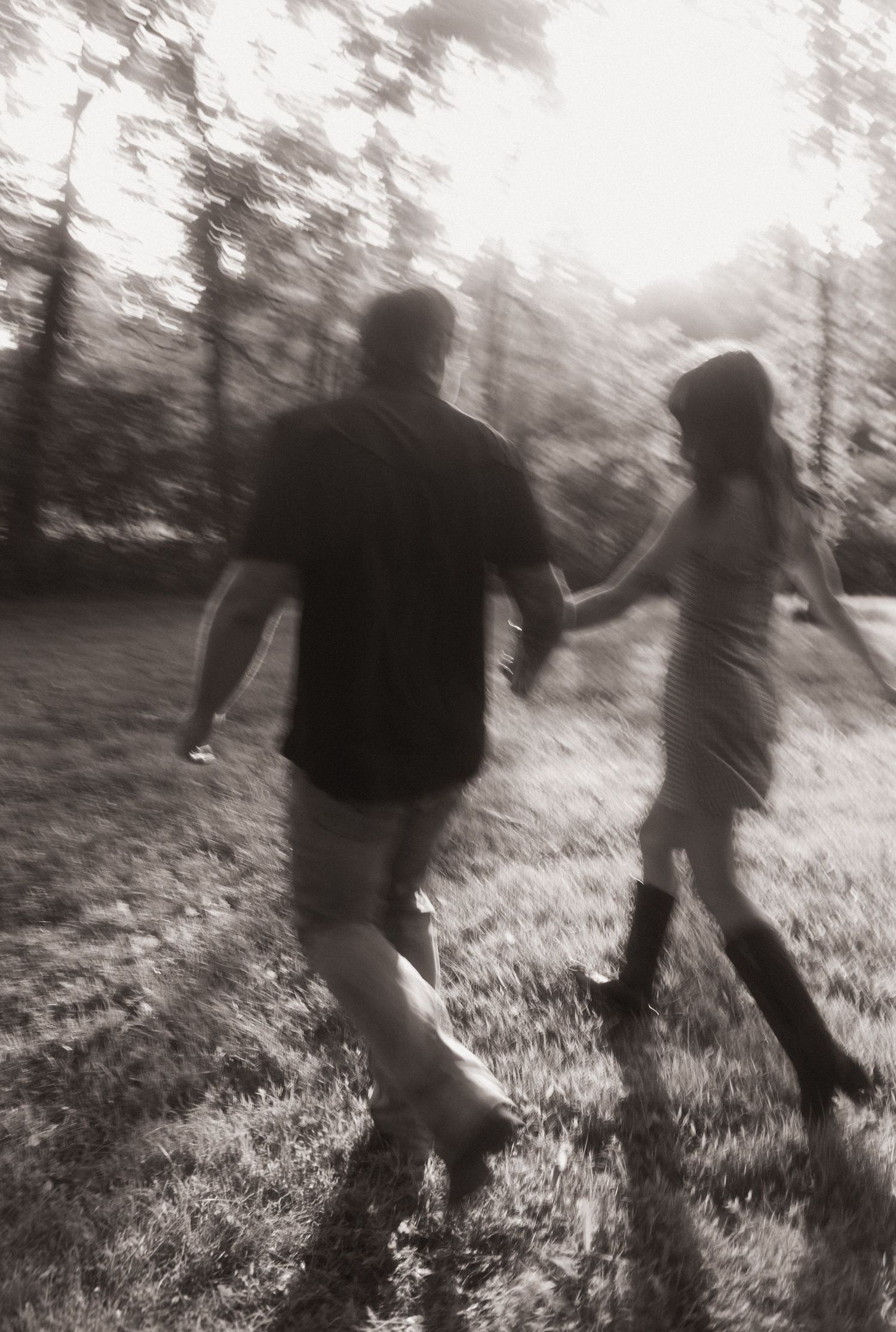 Blurry black and white photo of a couple holding hands while walking through a sunlit forest.