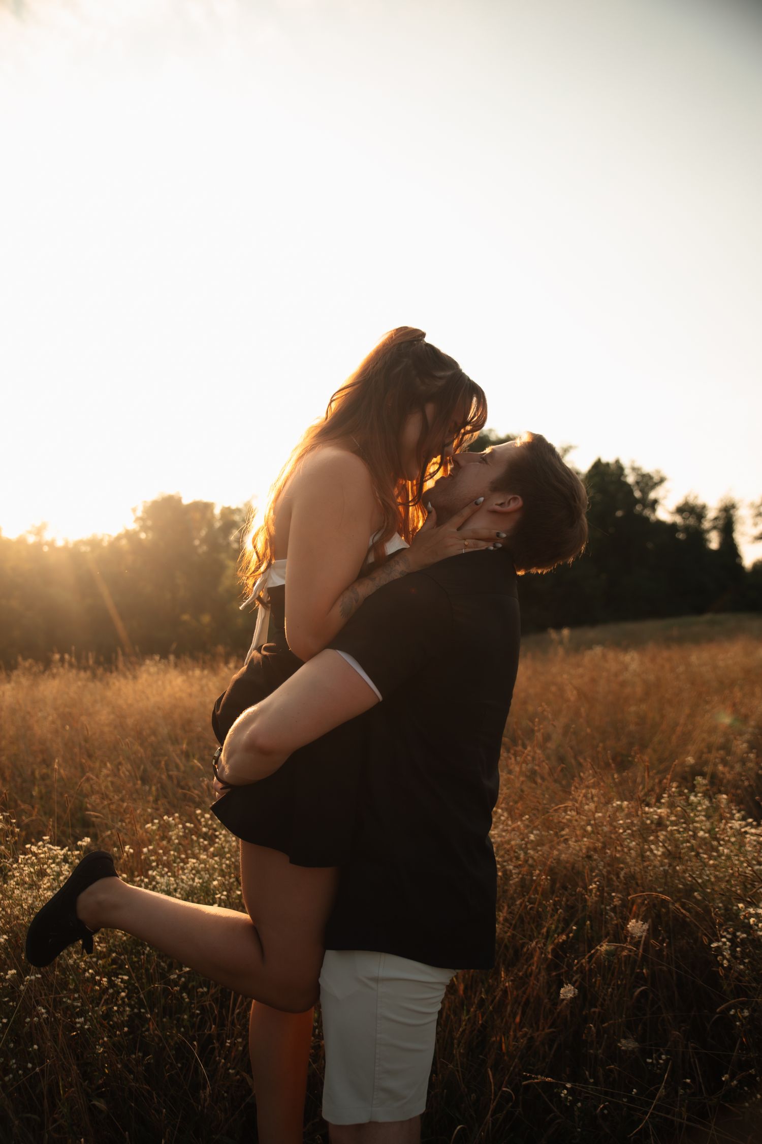 A romantic couple embraces in a golden sunlit field during sunset, creating a silhouette against the warm sky.