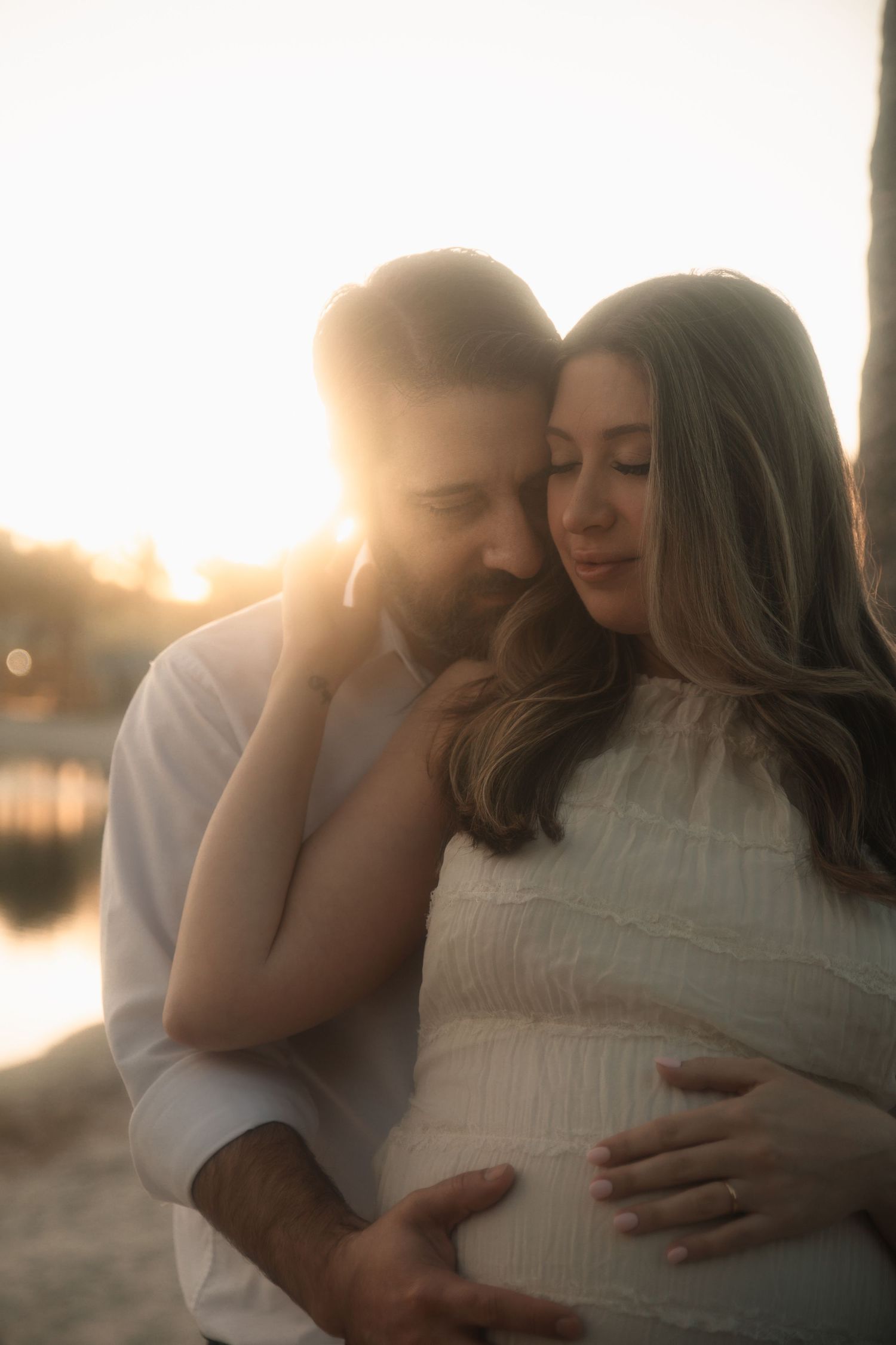 A romantic couple embraces during sunset by a lake in a series of intimate outdoor photos.