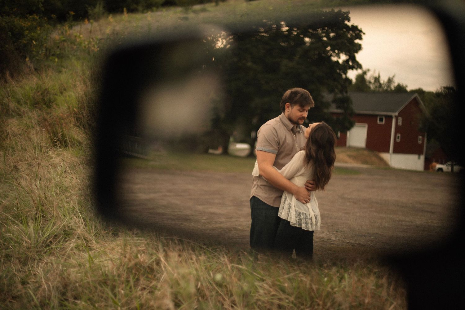 A romantic couple embraces on a dirt path at sunset, viewed through a soft vignette effect.