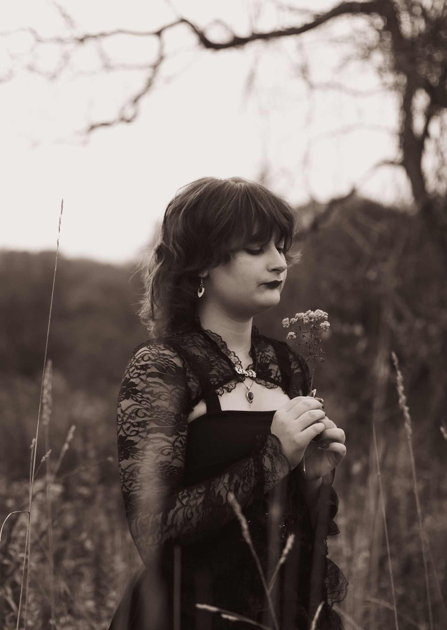 A person in dark clothing stands in a field of tall grass and wildflowers on an overcast day.