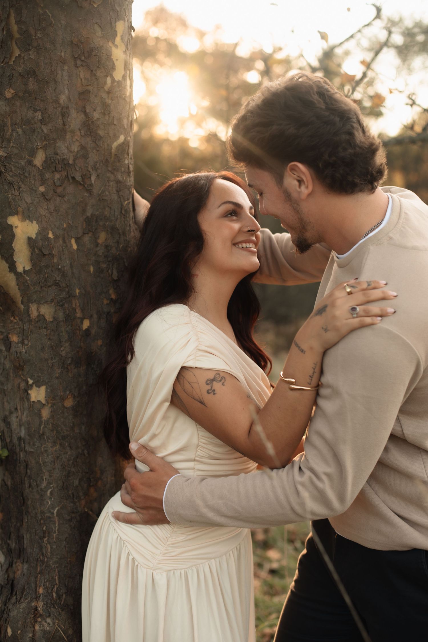 A romantic couple shares tender moments at sunset in a wooded setting wearing light colored outfits.
