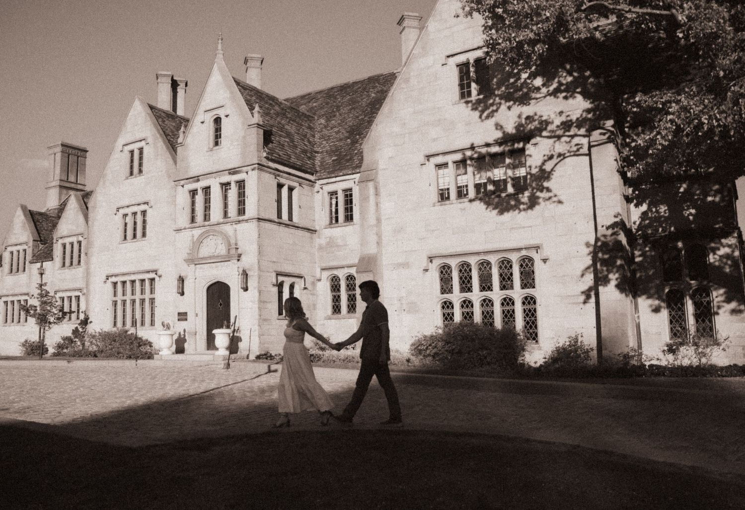 A romantic couple dances on the lawn in front of a grand Gothic Revival mansion in black and white photography.