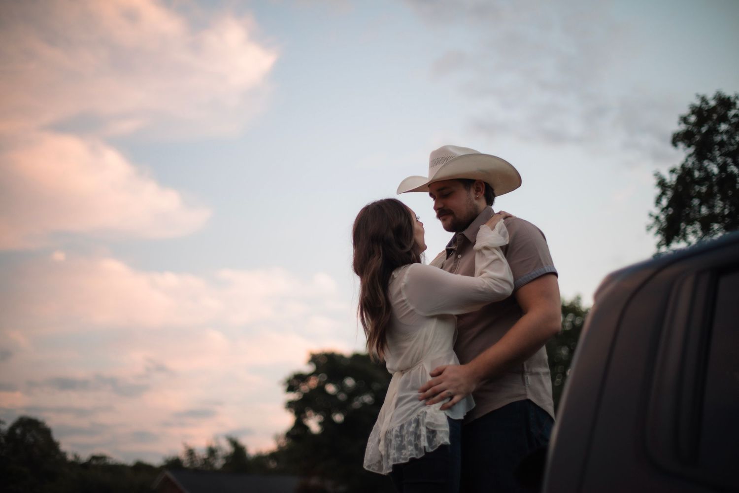 A couple in wedding attire share a romantic embrace at sunset in a scenic outdoor setting.