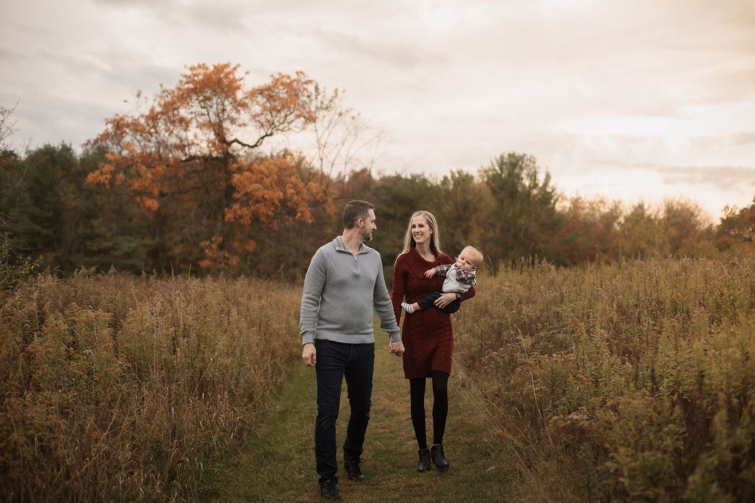 A family walks together through a rustic field during golden hour with fall colors in the background.