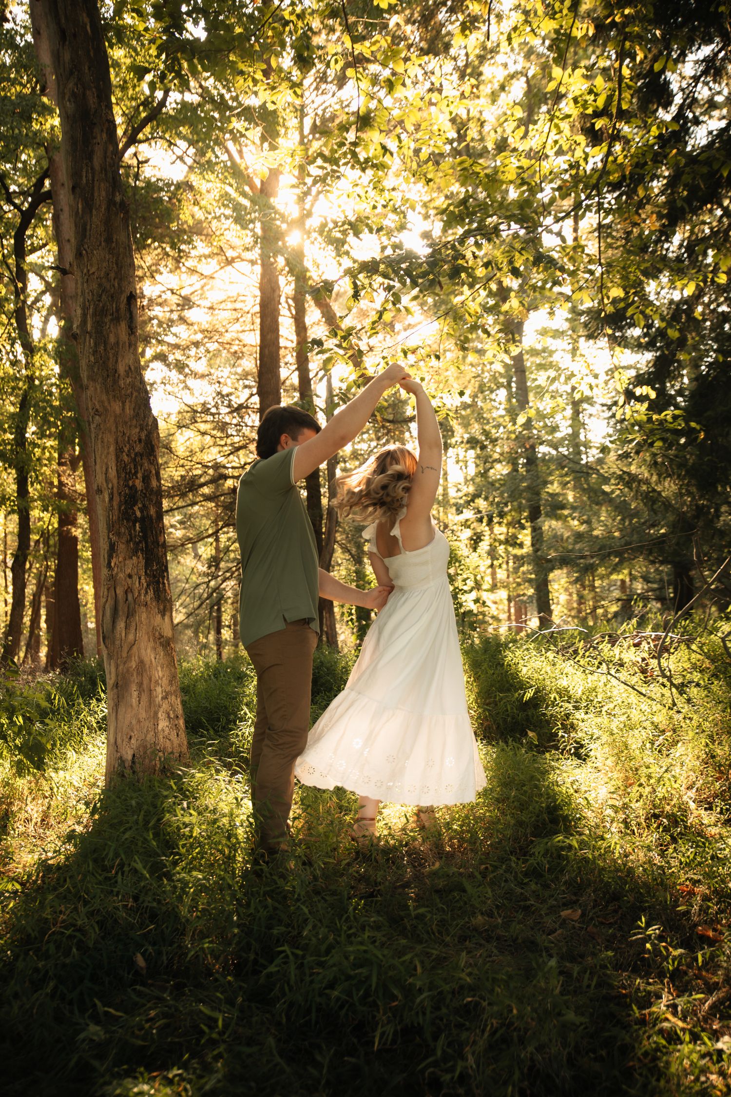 Sunlit forest scene with couple dancing among trees during golden hour.