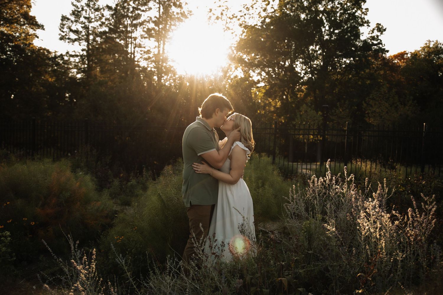 Romantic silhouettes embrace in a golden sunlit meadow during sunset creating a dreamy outdoor portrait.