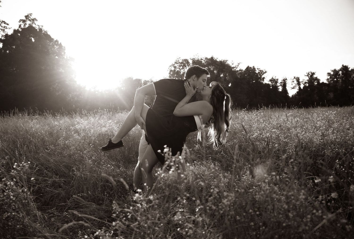 A silhouetted couple embraces in a sunlit meadow at golden hour creating a romantic black and white scene.