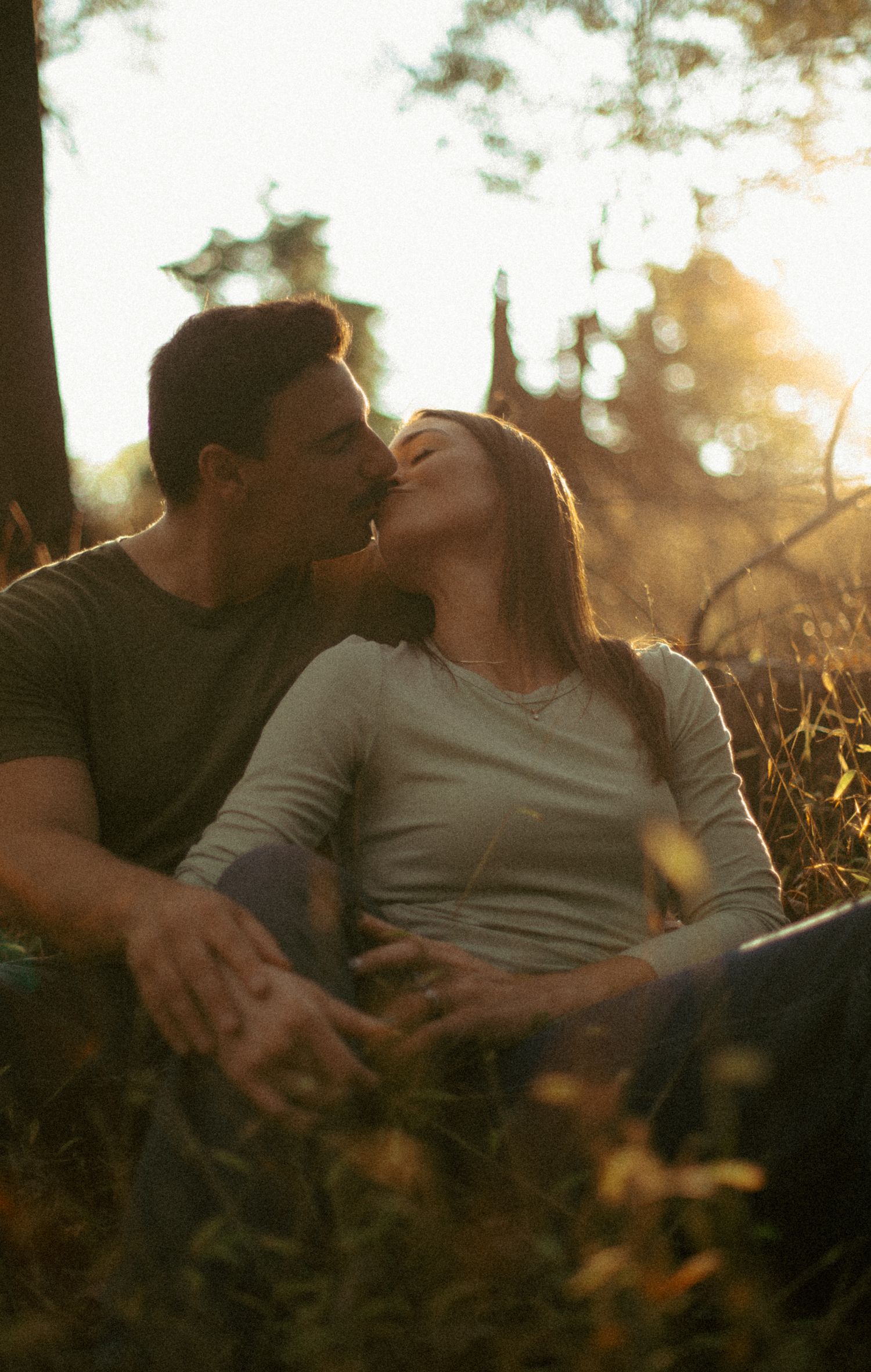 A couple shares an intimate moment in a sunlit meadow during golden hour as tall grass surrounds them.