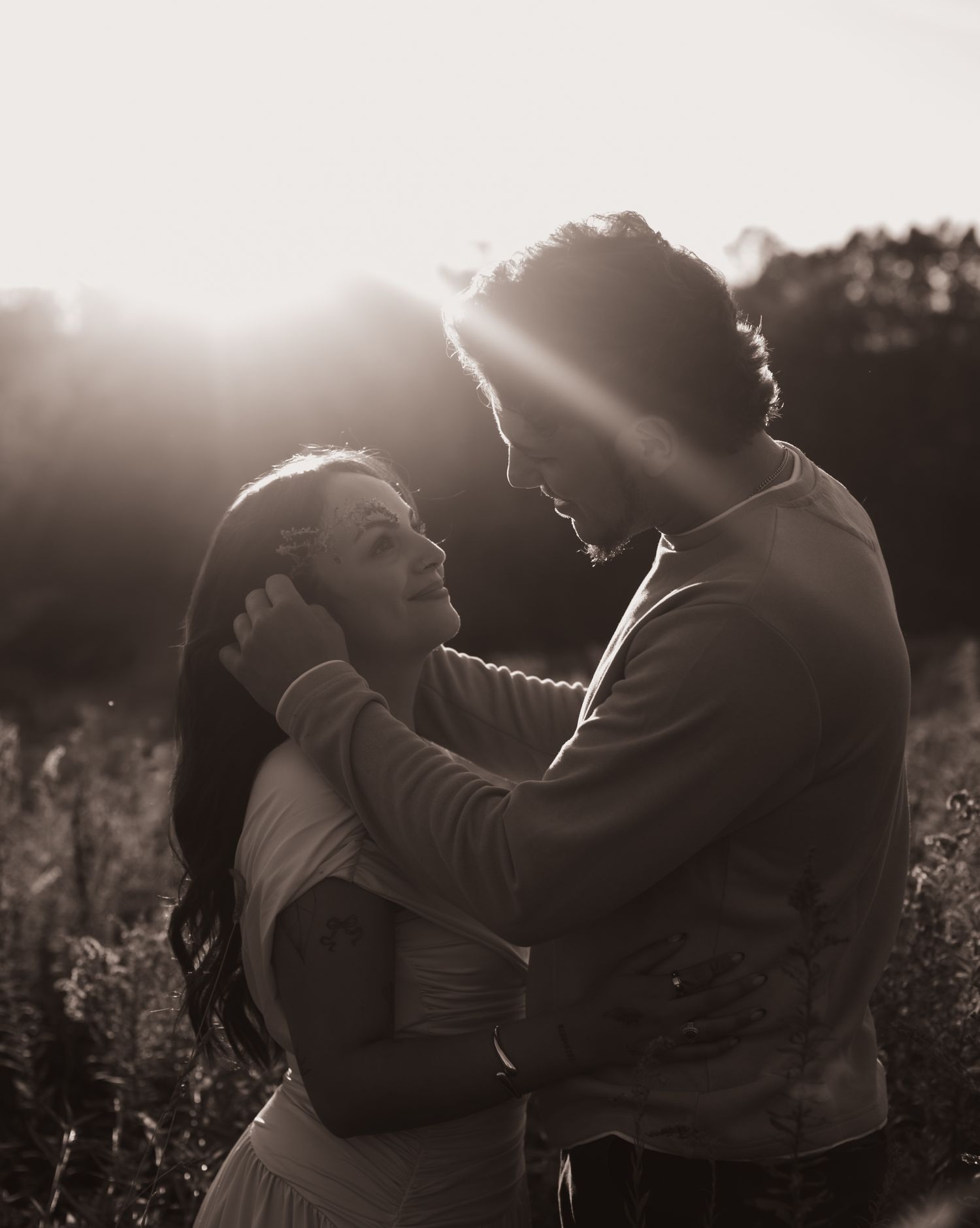Silhouetted couple embraces in golden sunlight during outdoor photo session in a field at sunset.