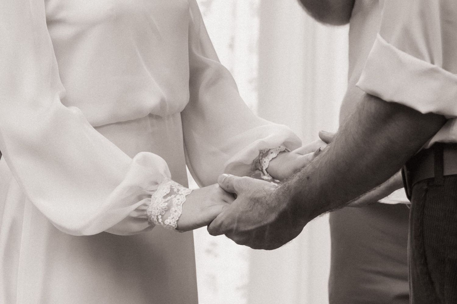 Black and white photo of a couple exchanging rings during a wedding ceremony, holding hands tenderly.