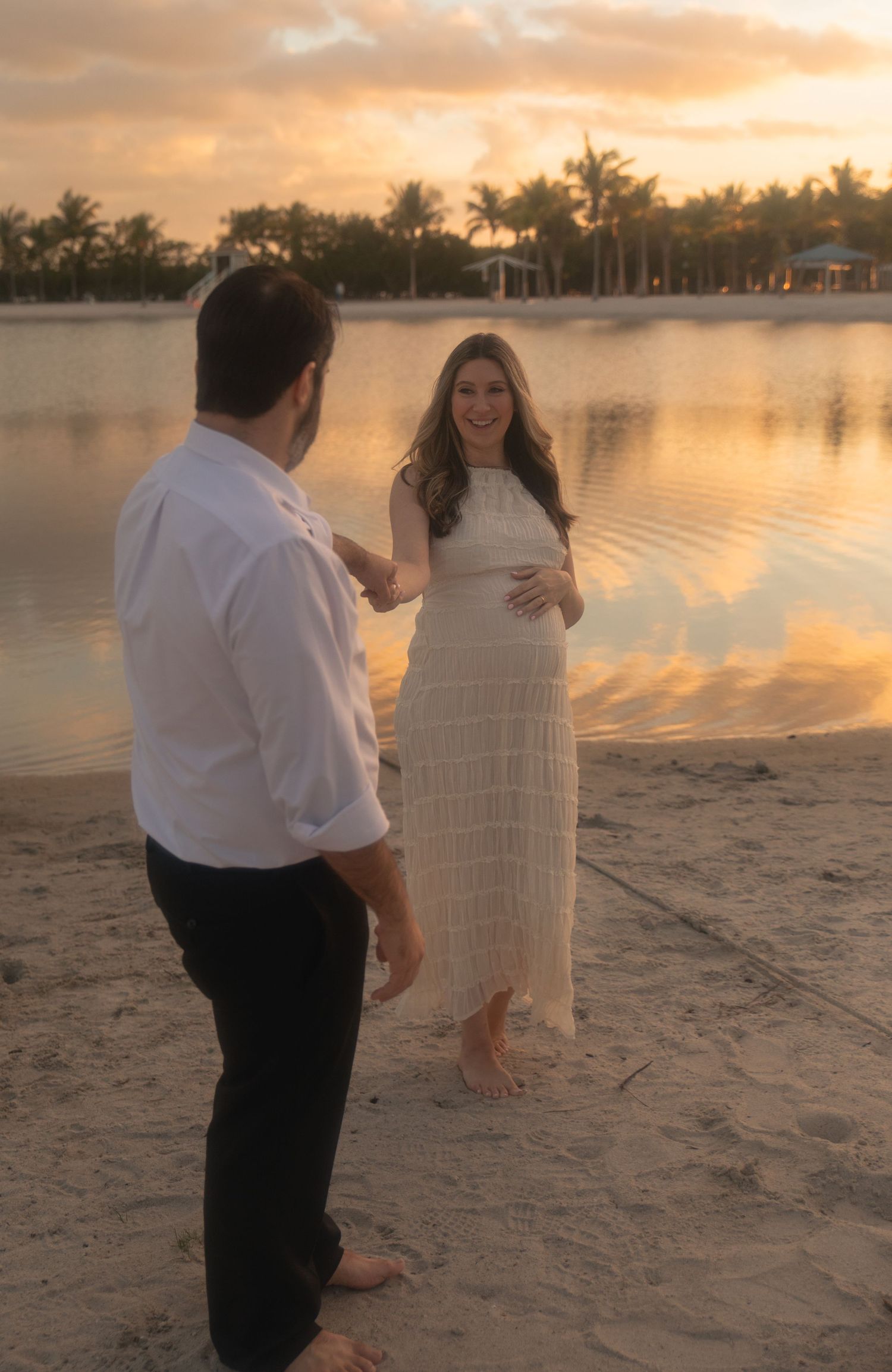 A romantic beach proposal scene at sunset with palm trees and calm waters in the background.
